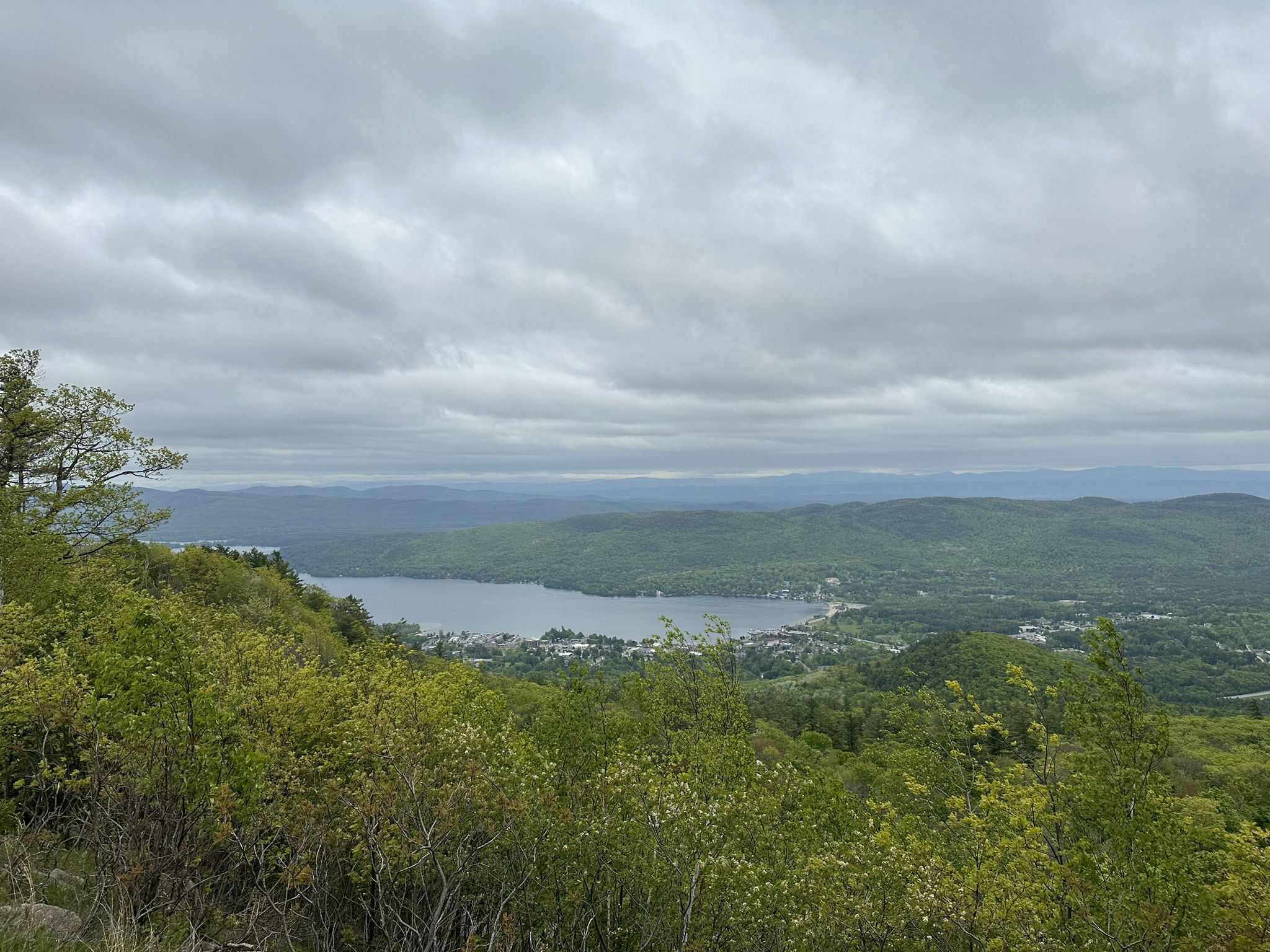 Overcast aerial view of a lake, town, and forested hills from a high vantage. - Prospect Mountain Trail