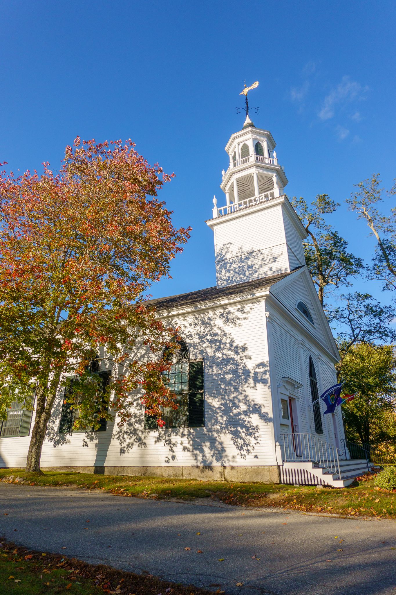 White church with steeple and autumn tree under a bright blue sky. - Blue Hill and Castine Figure-8 from Surry