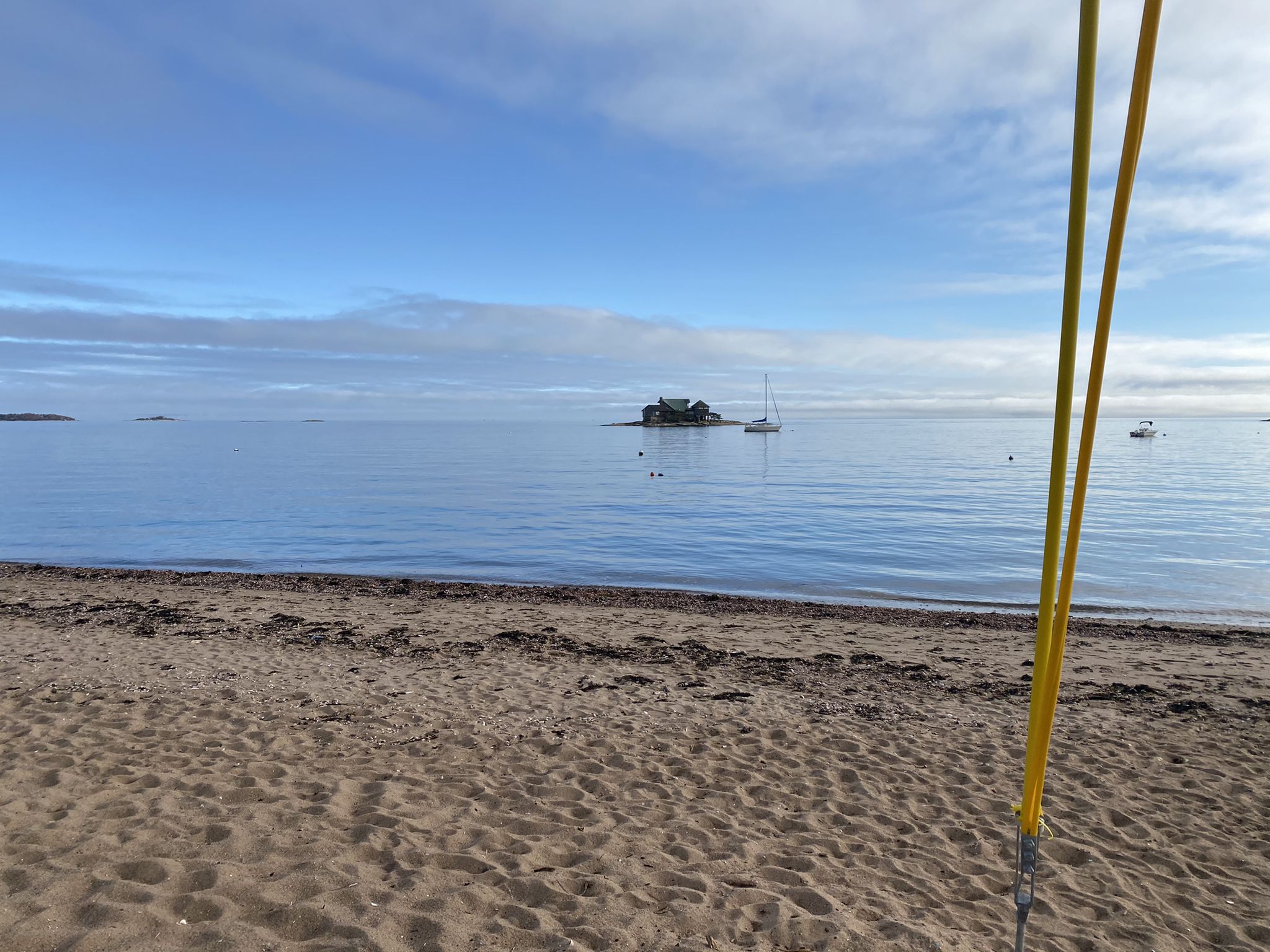 Sandy beach with calm ocean, distant island house, and sailboat under blue sky. - Limewood Avenue & Hotchkiss Cove Beach loop
