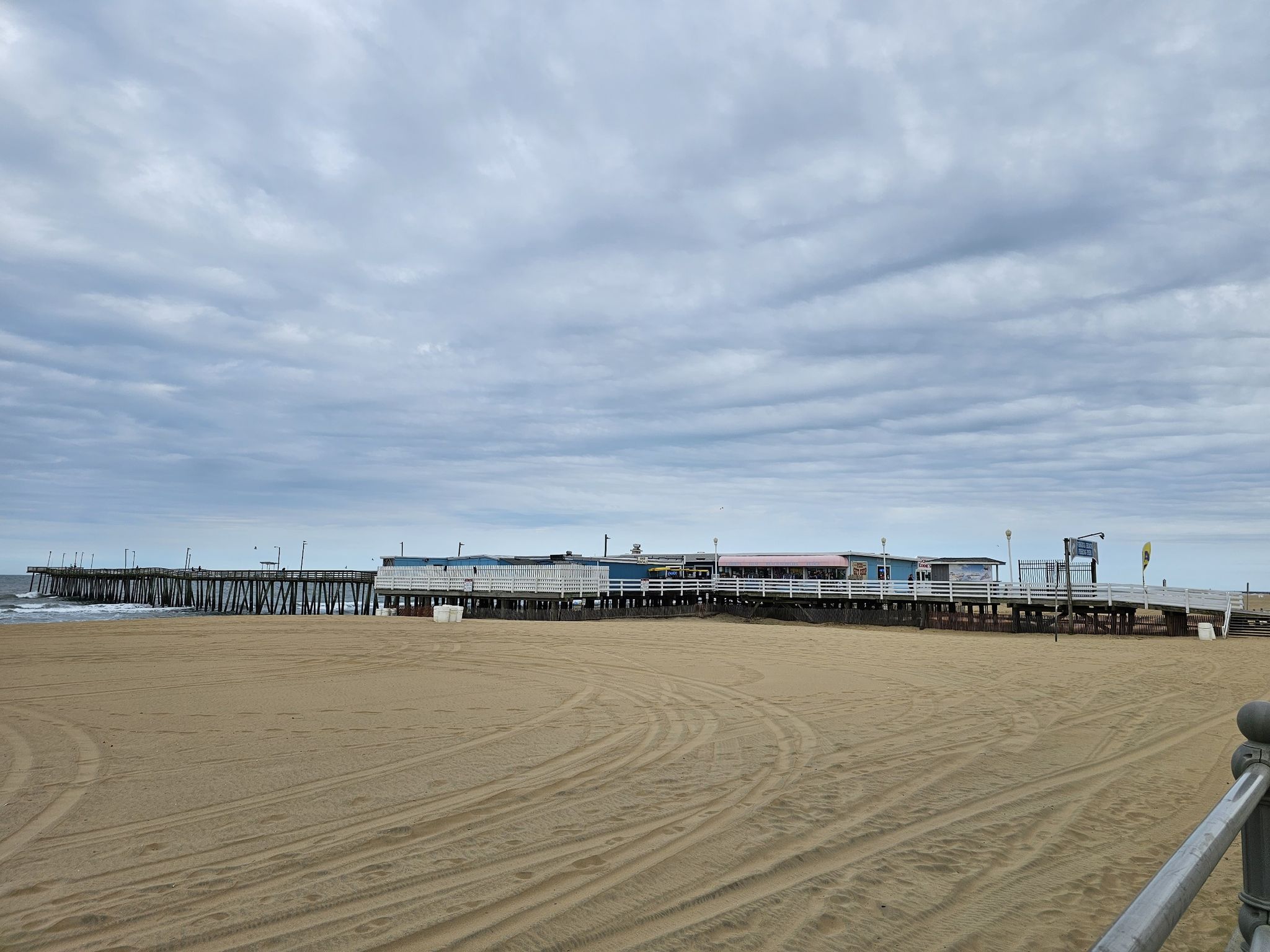 Sandy beach foreground with a long pier and buildings under a cloudy sky. - Fishing Pier – Virginia Beach Boardwalk loop from Virginia Beach