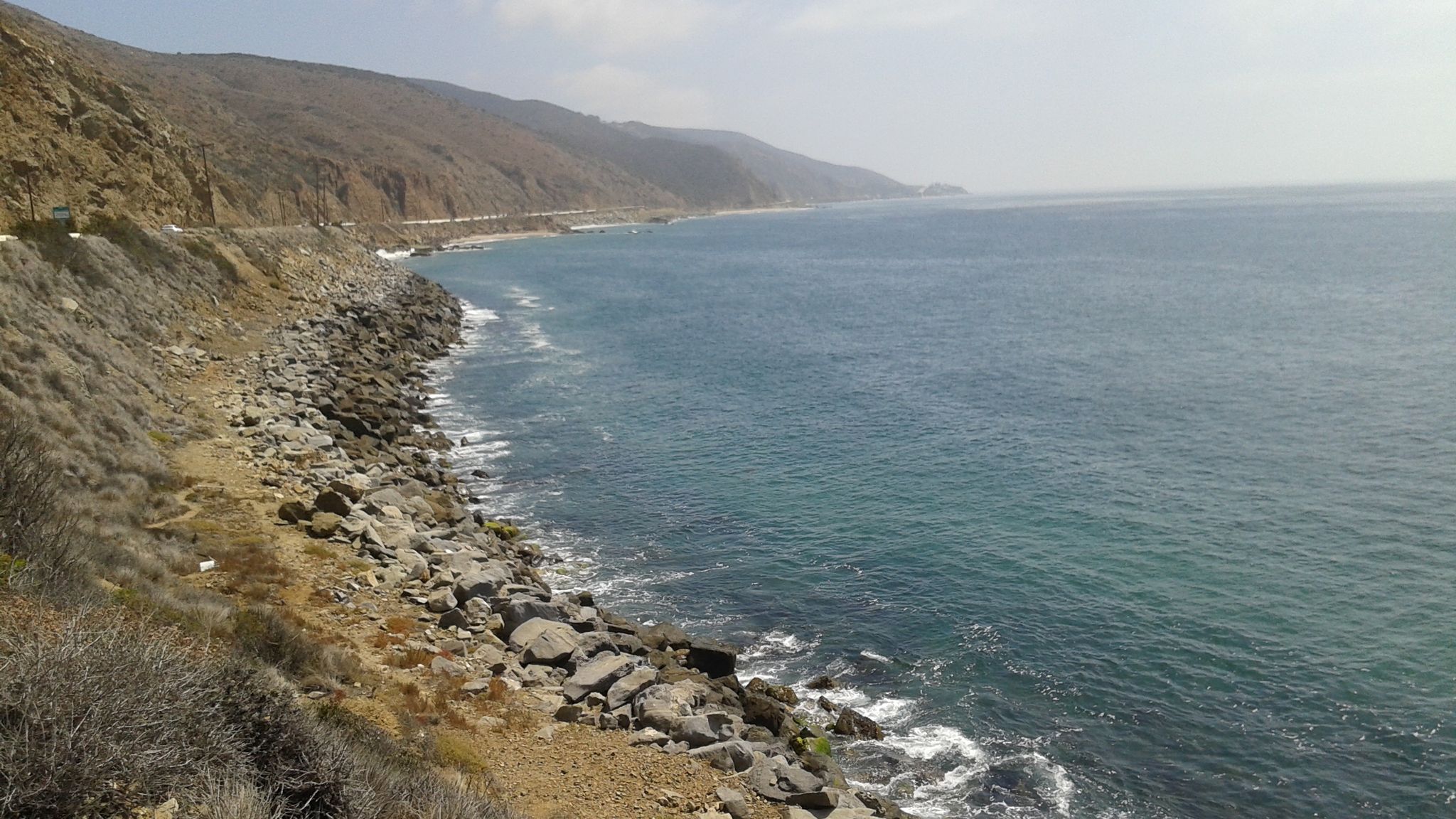Rocky coastline with crashing waves, a road, and distant mountains. - Sandstone Peak Trailhead – Leo Carrillo State Park Beach loop from Santa Monica Mountains National Recreation Area - Service Area