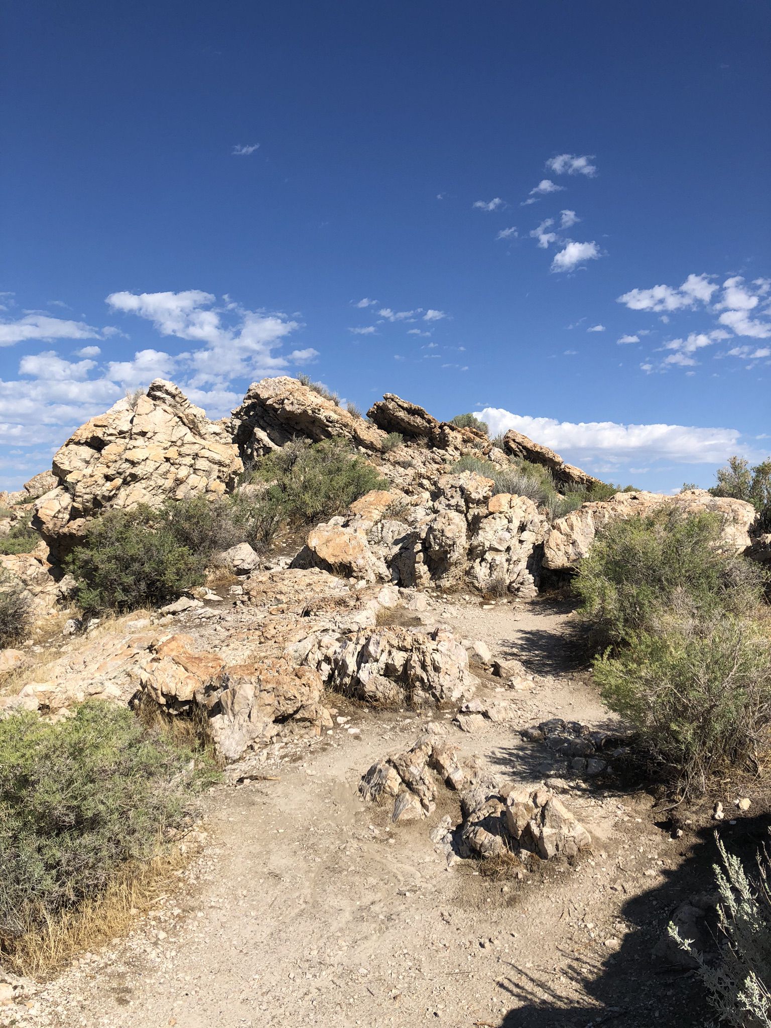 Jagged rocky outcrop with a winding dirt path under a bright blue sky. - Antelope Island Road & Lady Finger Point Trail loop