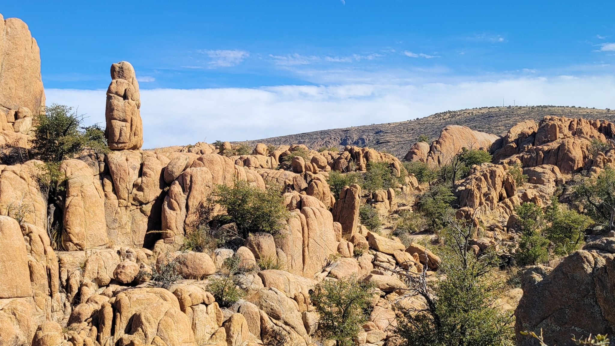 Tall rock formation amidst a rugged, sunlit desert landscape under blue sky. - Captain‘s Trail – Iron King Trail loop from Vista Park