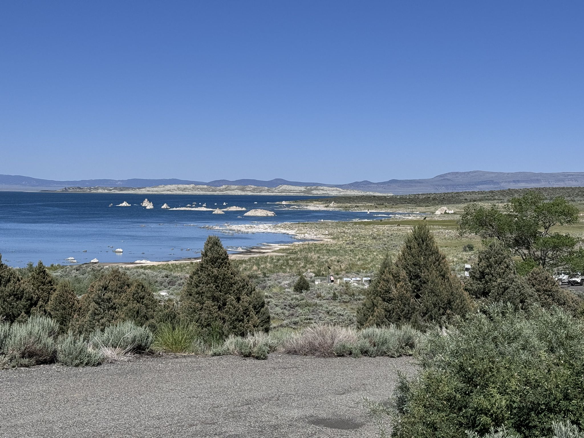 Bright lake with tufa rock formations, sparse shoreline, and distant mountains under clear sky. - Lee Vining to Lundy Lake