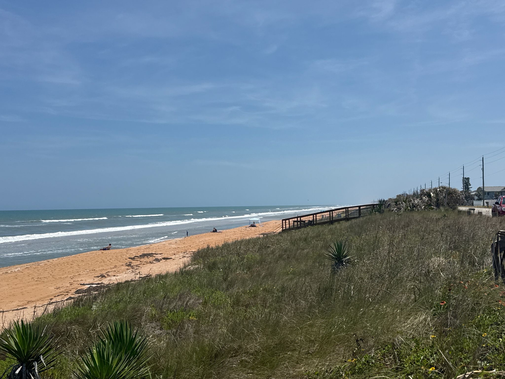 Sunny beach with ocean waves, grassy dunes, and a boardwalk under blue sky. - Ormond Beach to Flagler Beach Scenic Drive
