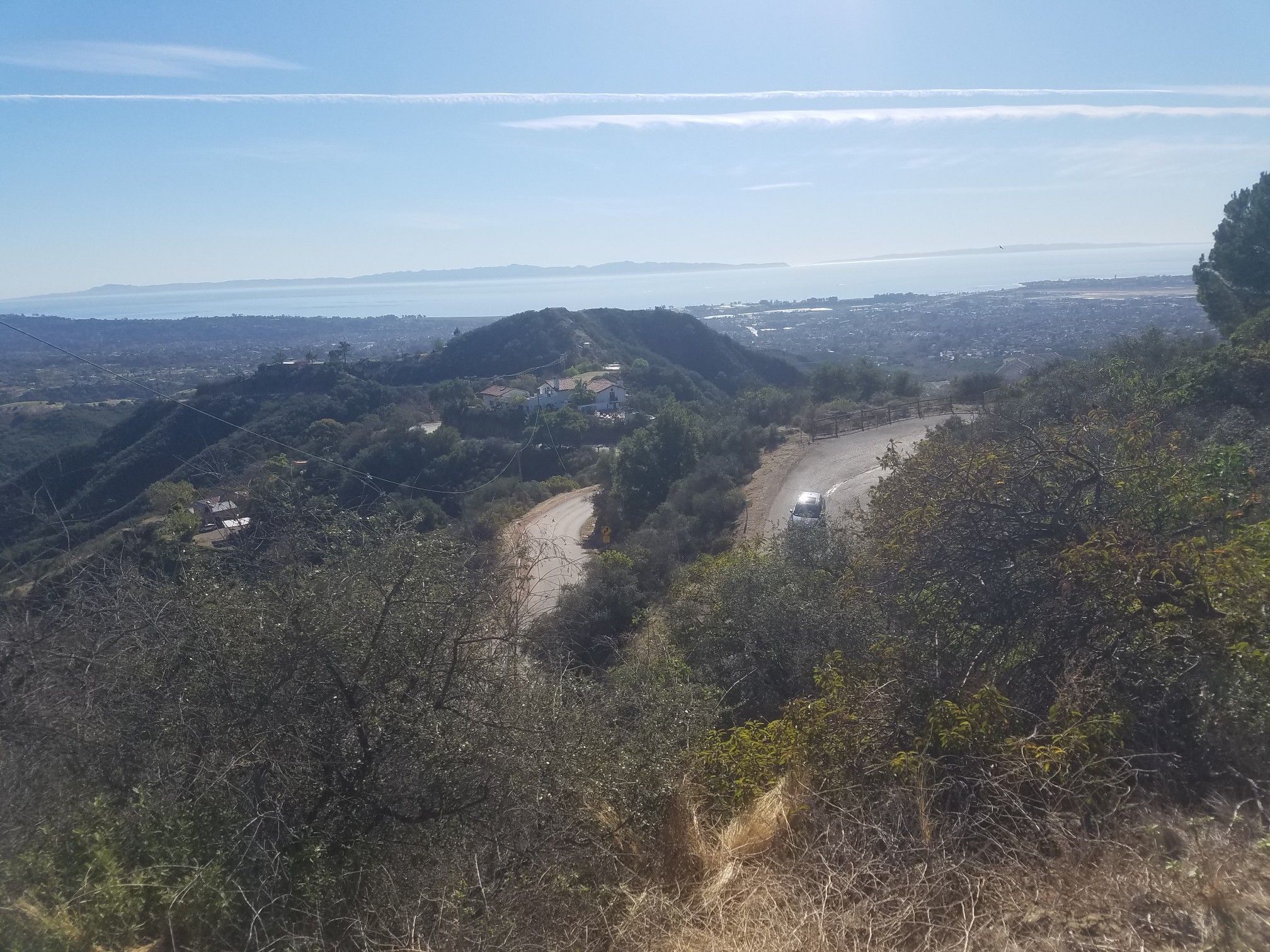 Sunny view of a winding road through green hills with a distant city. - El Capitan State Beach – Cold Spring Arch Bridge - National Landmark loop from Goleta