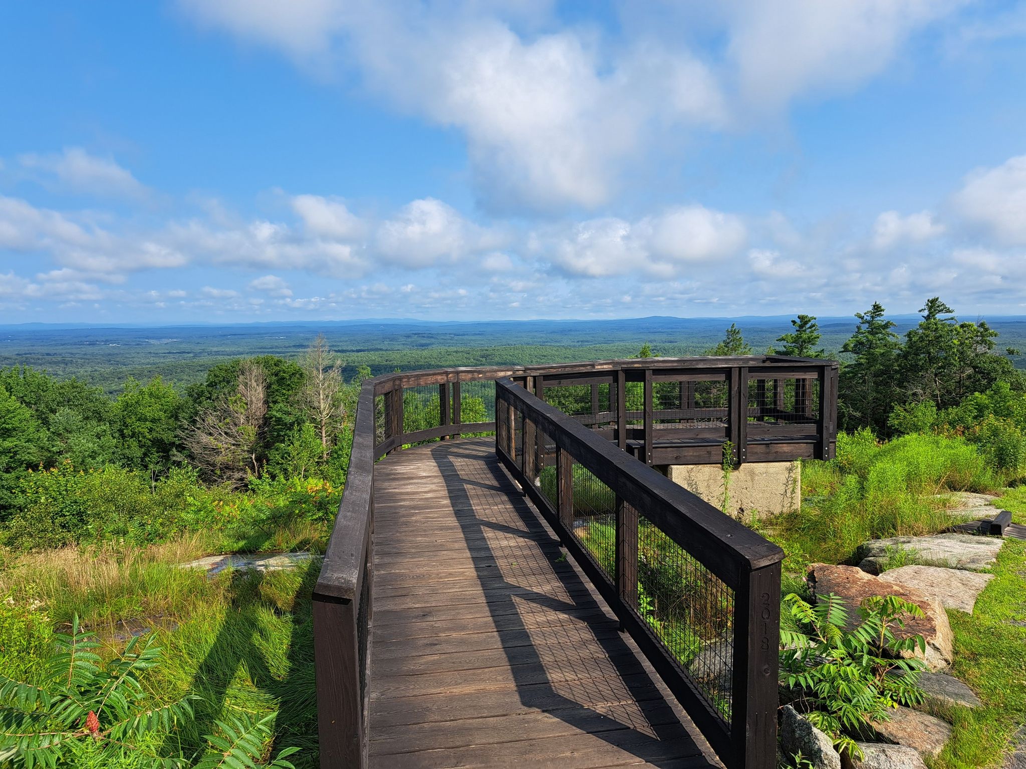 Wooden observation deck overlooks a vast green forest under a sunny blue sky. - Second Hill via Sweet Fern Trail