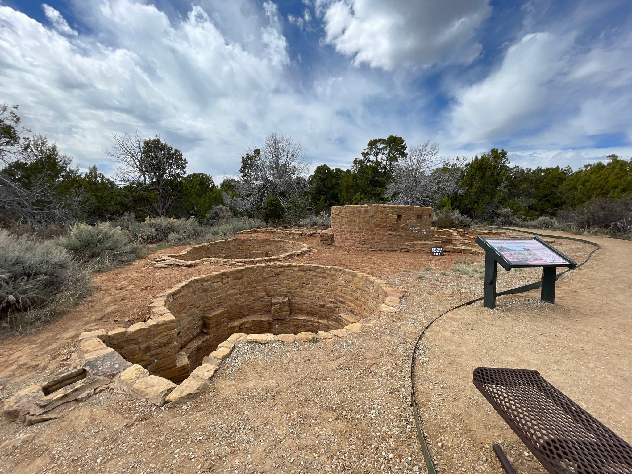 Multiple stone ruins and an informational sign in a dry, cloudy landscape. - Far View Sites Trail