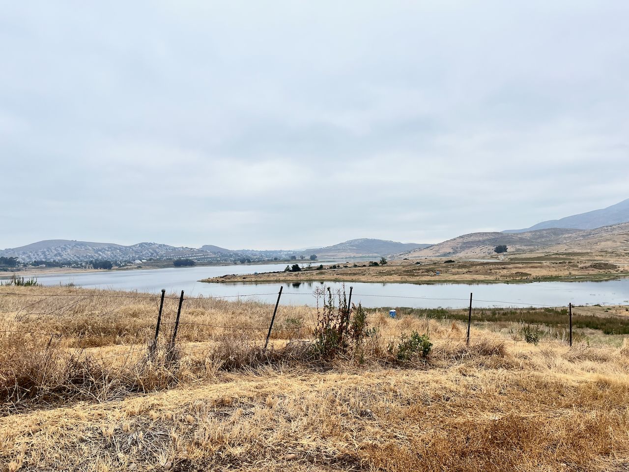 Overcast sky above a lake surrounded by dry, golden hills and a fence. - Mother Miguel Mountain via Sweetwater Park
