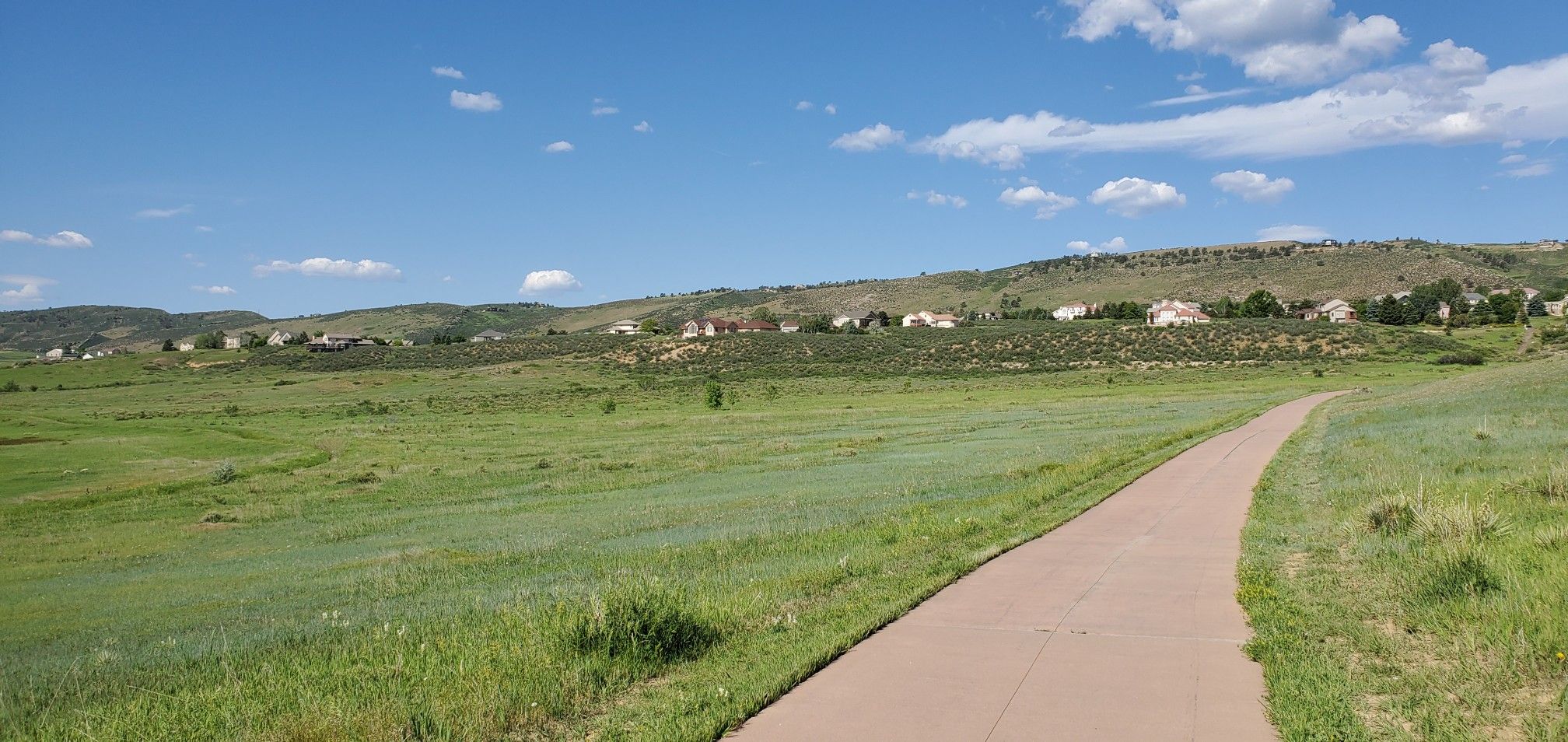 Paved path through green fields, houses on distant sunny hills under blue sky. - Spring Creek, Fossil Creek, and Power Trail Loop