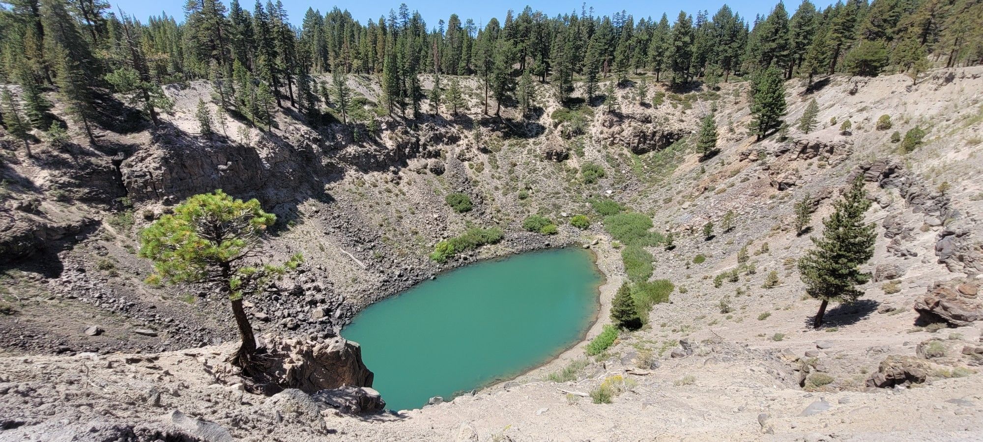 Bright turquoise lake nestled in a rocky crater, surrounded by pine trees. - Inyo Craters Trail