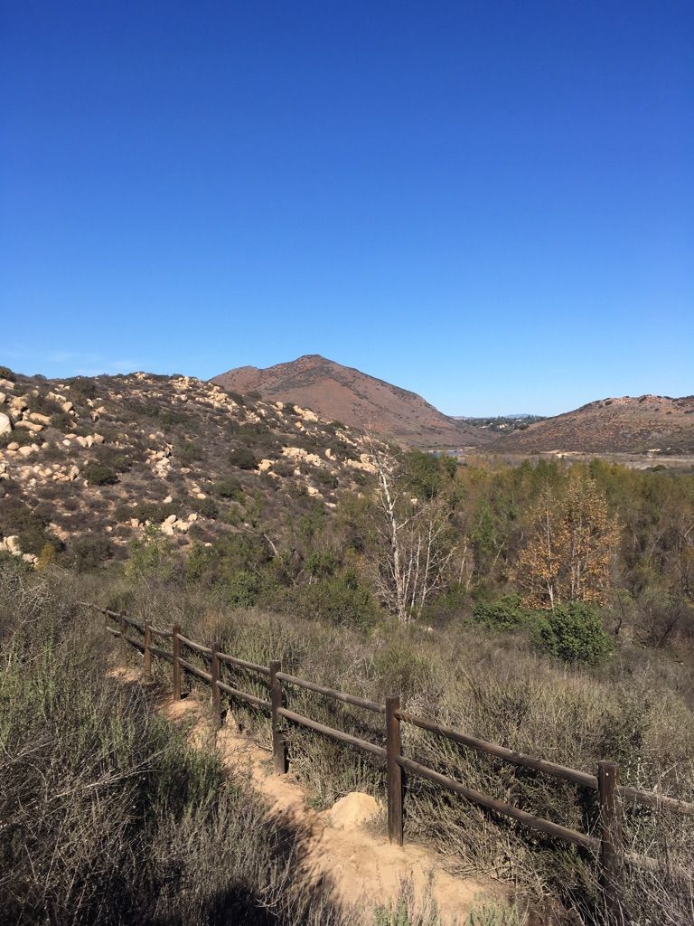 Dirt path with a wooden fence, leading towards distant mountains under clear sky. - Bernardo Bay – Small waterfall loop from Westfield North County