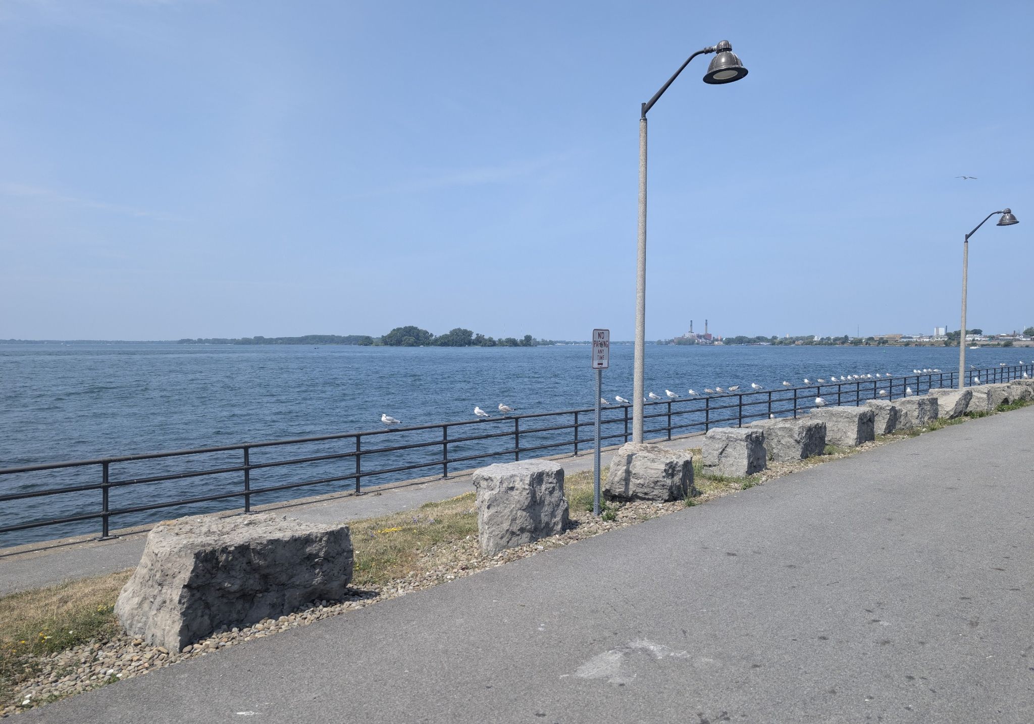 Paved waterfront path with a black fence, streetlights, and blue water. - Grand Island Loop