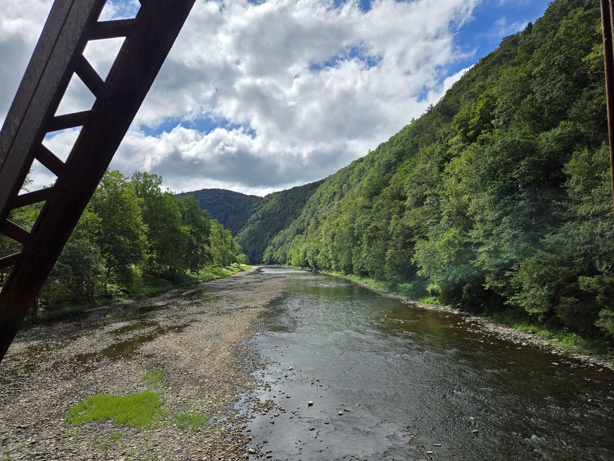 River with rocky banks, forested hills, and cloudy sky, viewed from a bridge. - Hoffman Campground loop from Cedar Run
