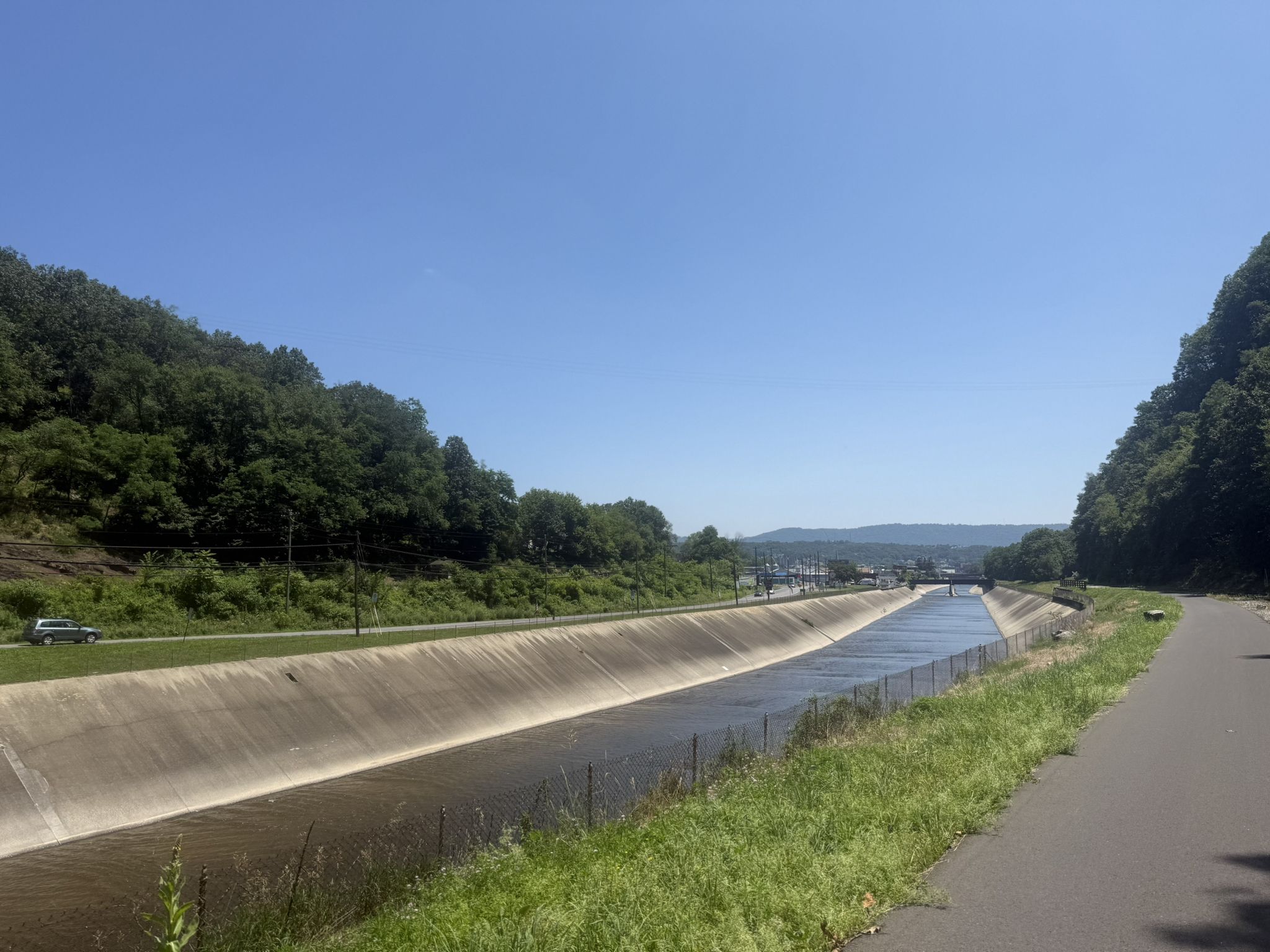 A canal with concrete banks next to a road, surrounded by green hills. - Helmstetter’s Curve – Brush Tunnel loop from Cumberland