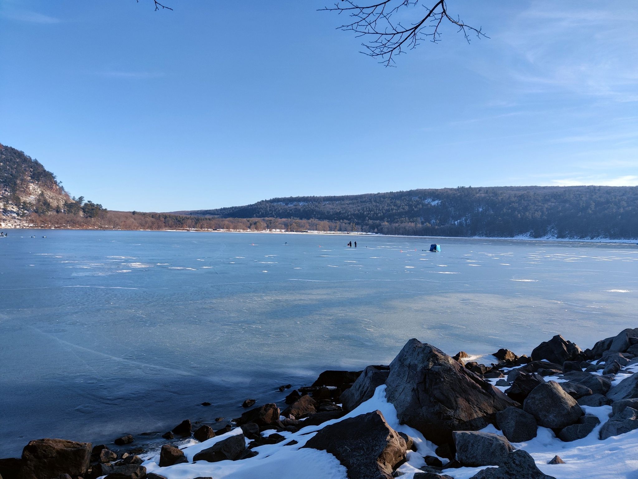 Sunny winter scene with frozen lake, snowy rocks, and distant hills. - Tumbled Rocks Trail