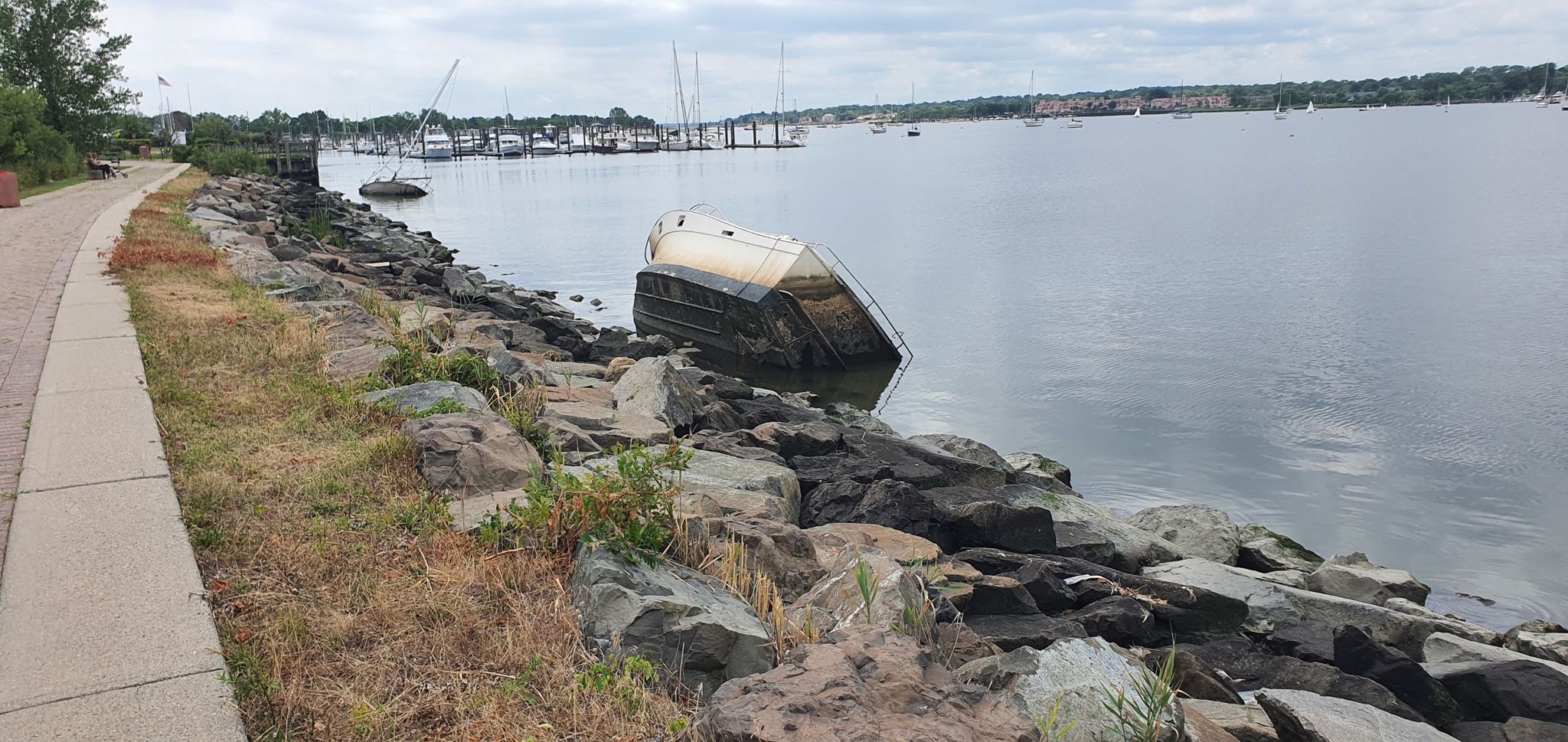 A partially submerged boat rests on a rocky shore next to calm water. - Great Kills Park Multi-Use Path