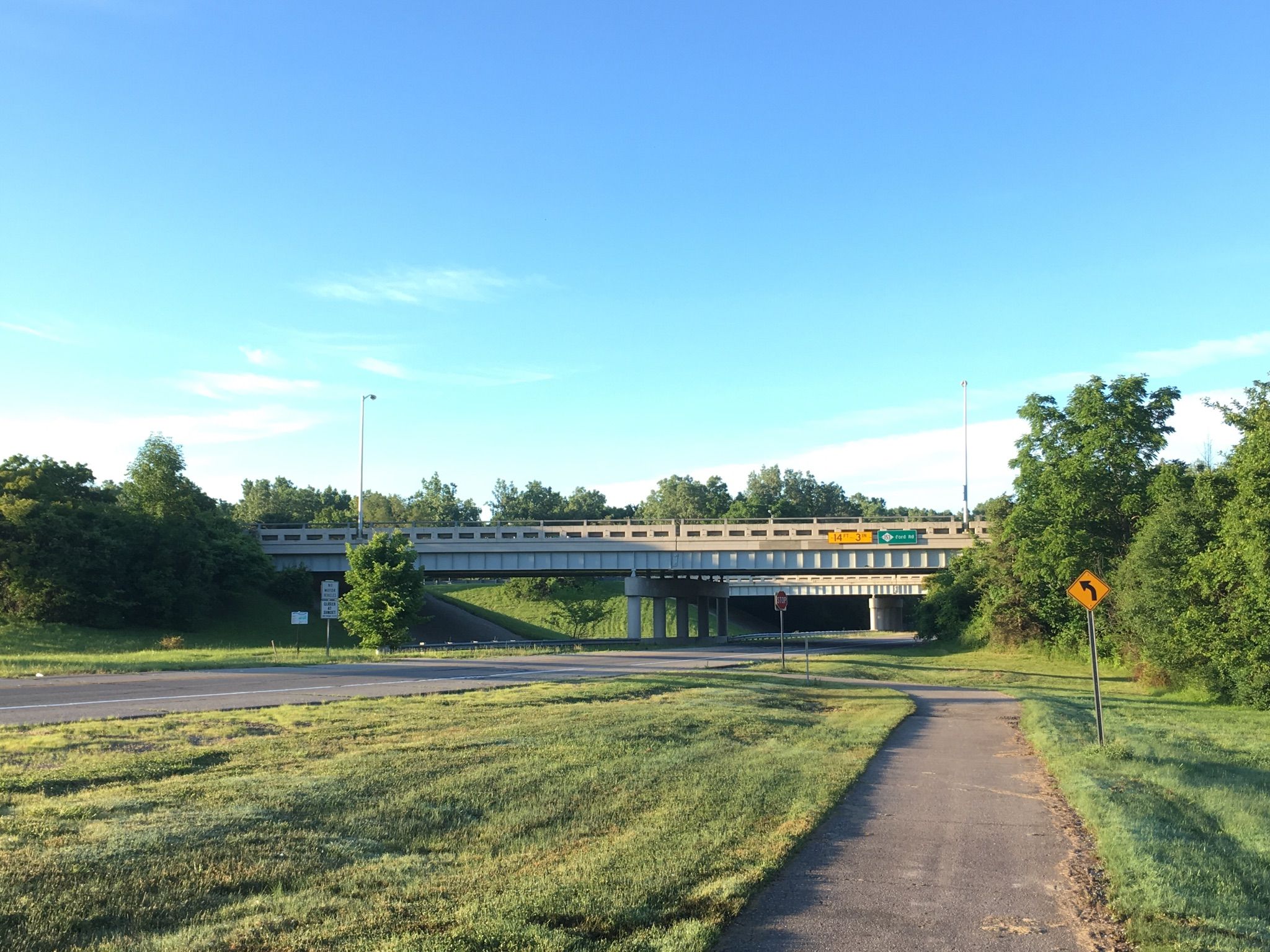 A large concrete overpass spans a road, with a paved path nearby. - Rouge River Gateway Trail