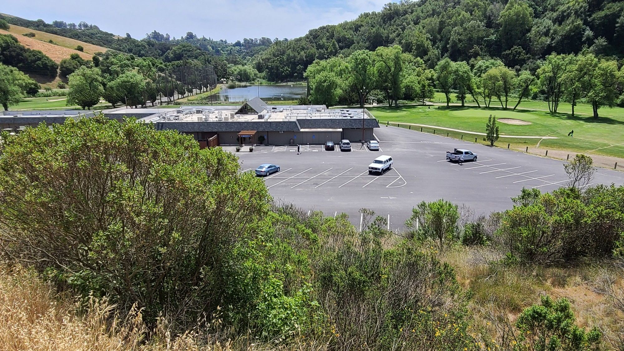 Building, parking lot, and golf course by a lake under bright skies. - Redtail and Brandon Skyline Trails loop