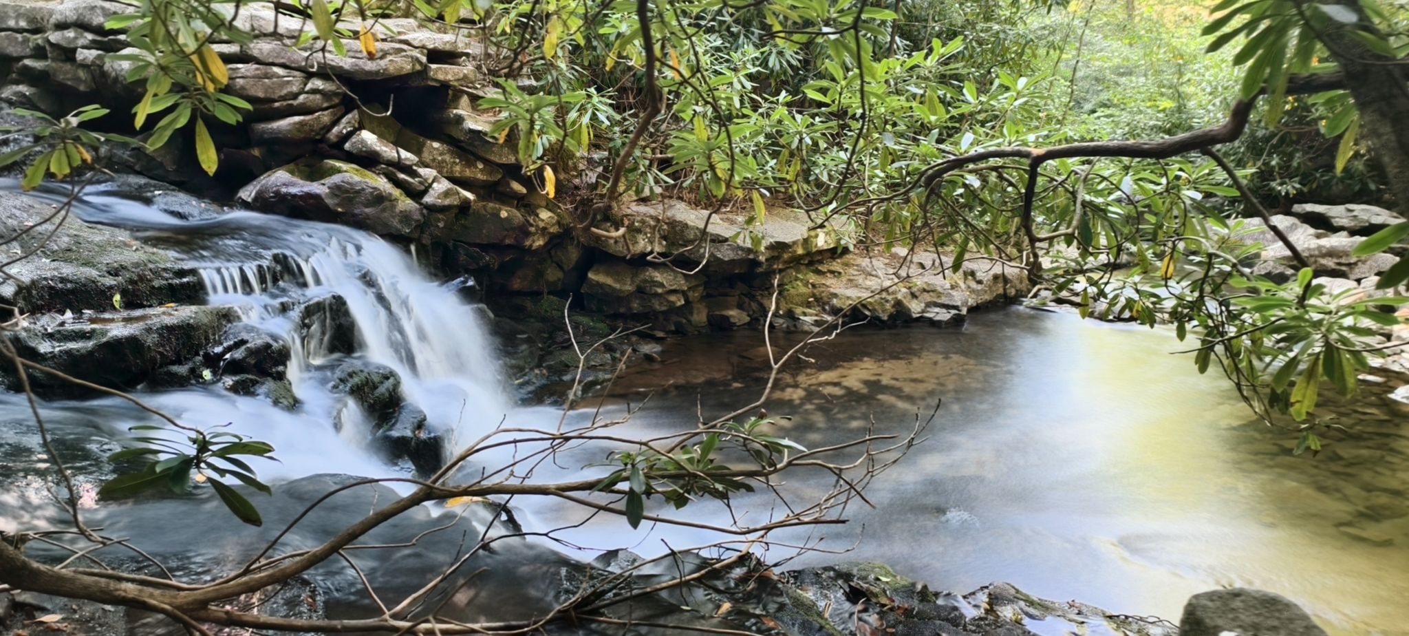 Cascading waterfall flows into a calm stream, framed by green branches. - Waterfall at Sand Spring Run Dam loop from Hickory Run