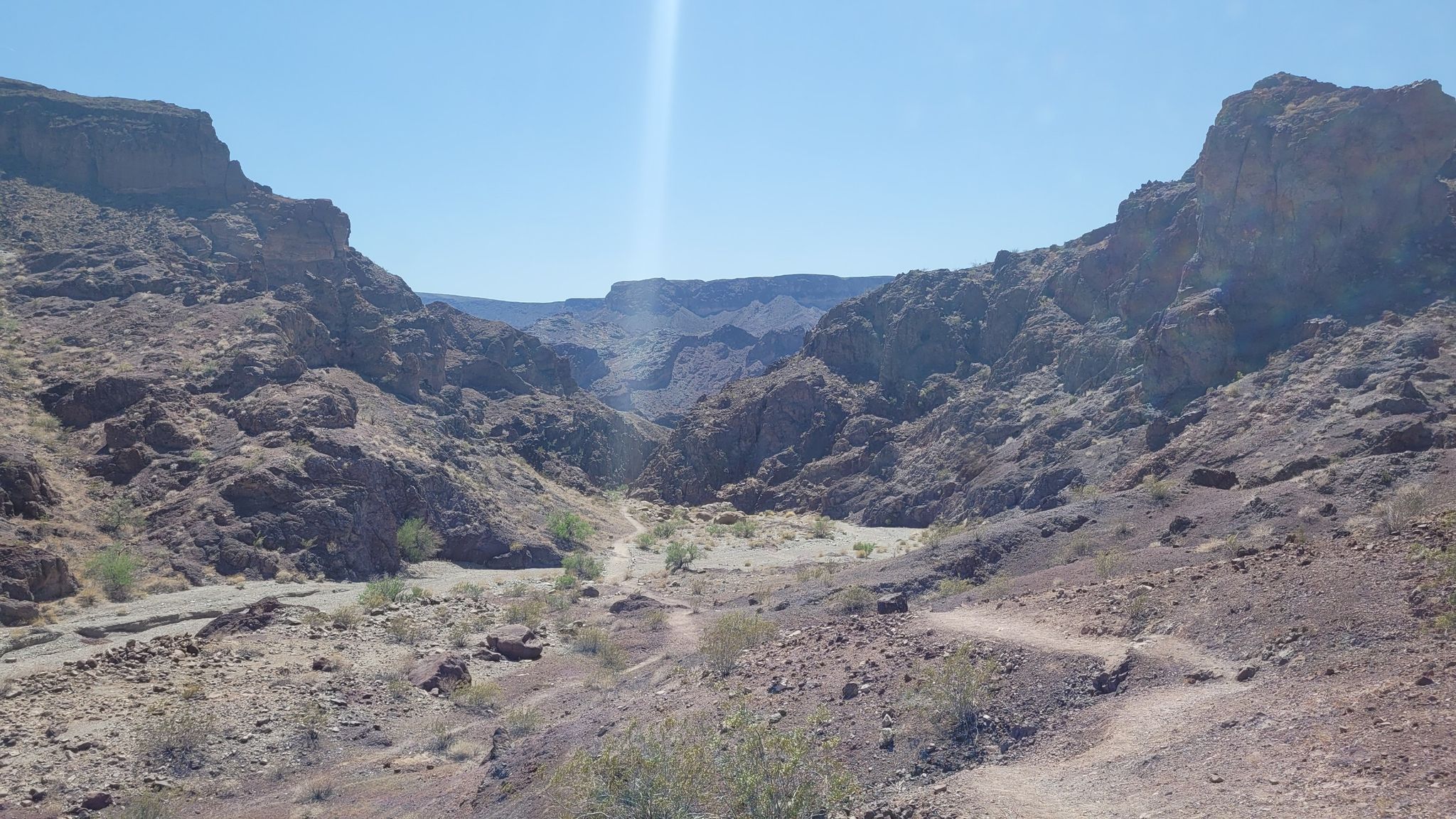 Expansive desert canyon with a winding trail and distant mountains under a bright sky. - Arizona Hot Spring Trail