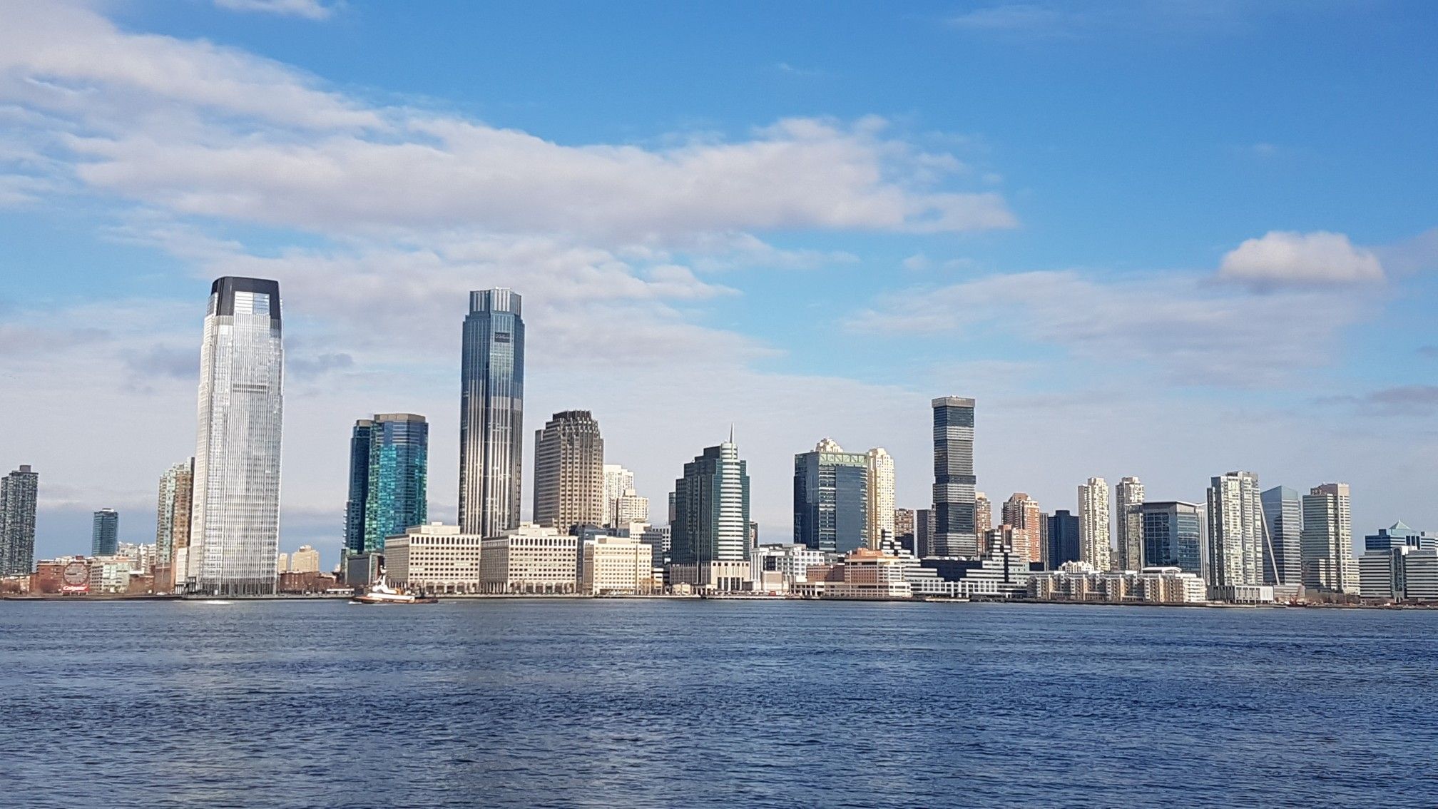 City skyline across calm water under a blue sky with white clouds. - North Cove Marina – Brookfield Place loop from New York