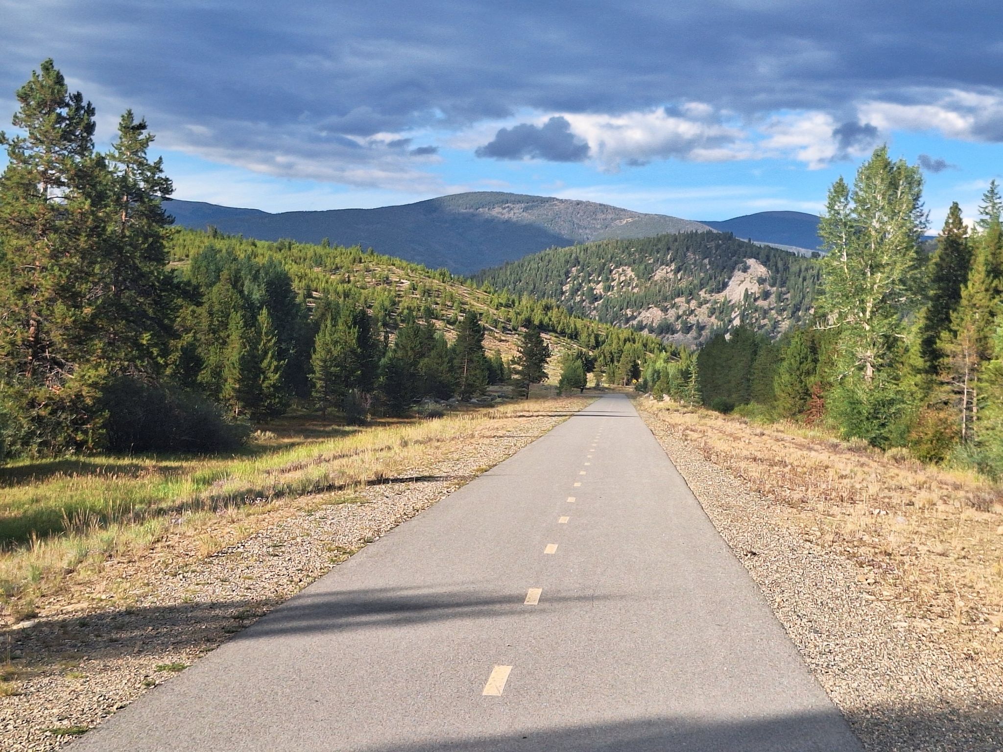 Straight paved road through grassy and forested hills with distant mountains under cloudy sky. - Lakeshore Perimeter and Crown Point Road Loop