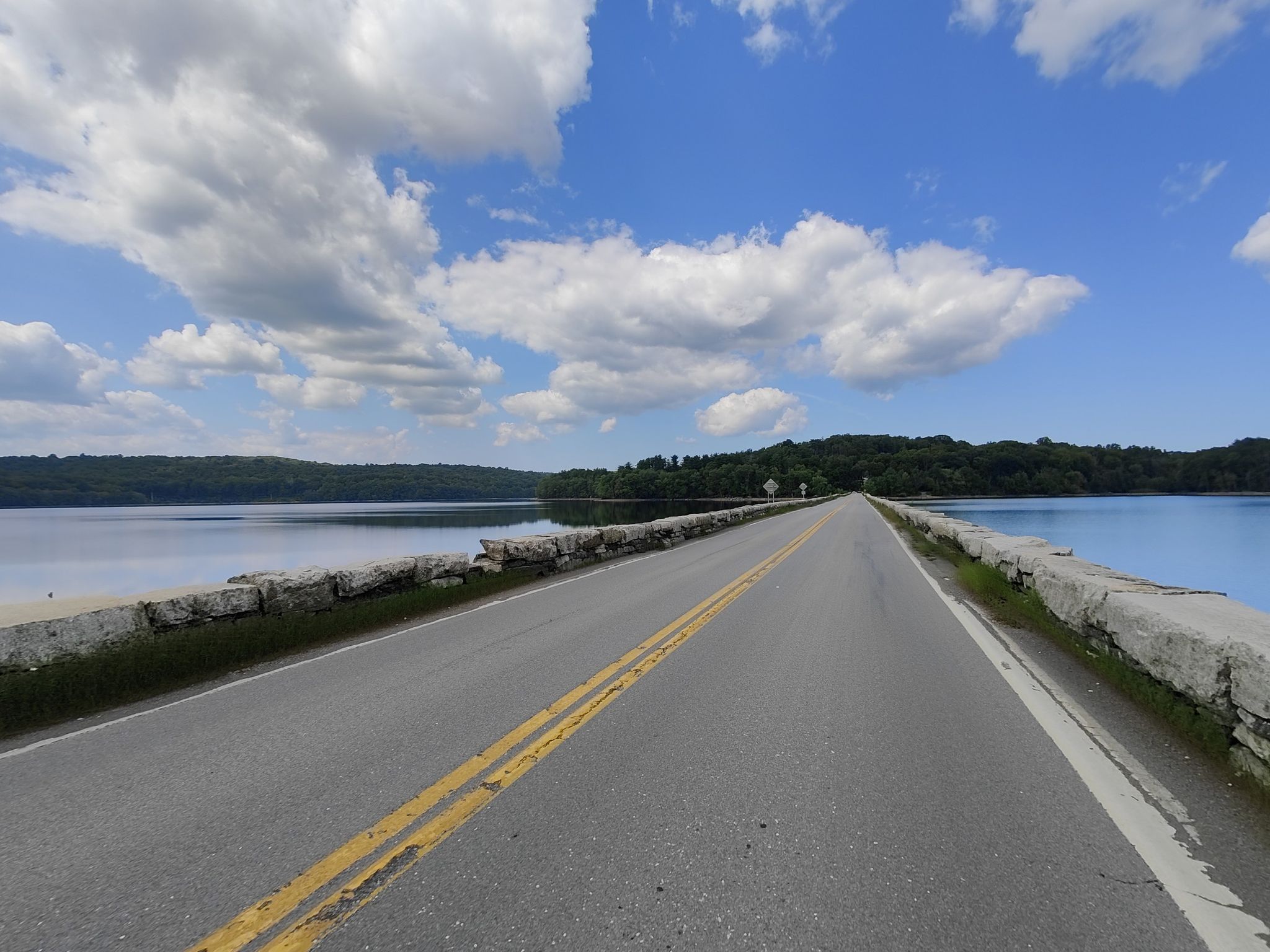 Straight road over a lake with forested banks under a bright, cloudy sky. - Titicus Reservoir South Side – Lovers Landing Bridge loop from Katonah
