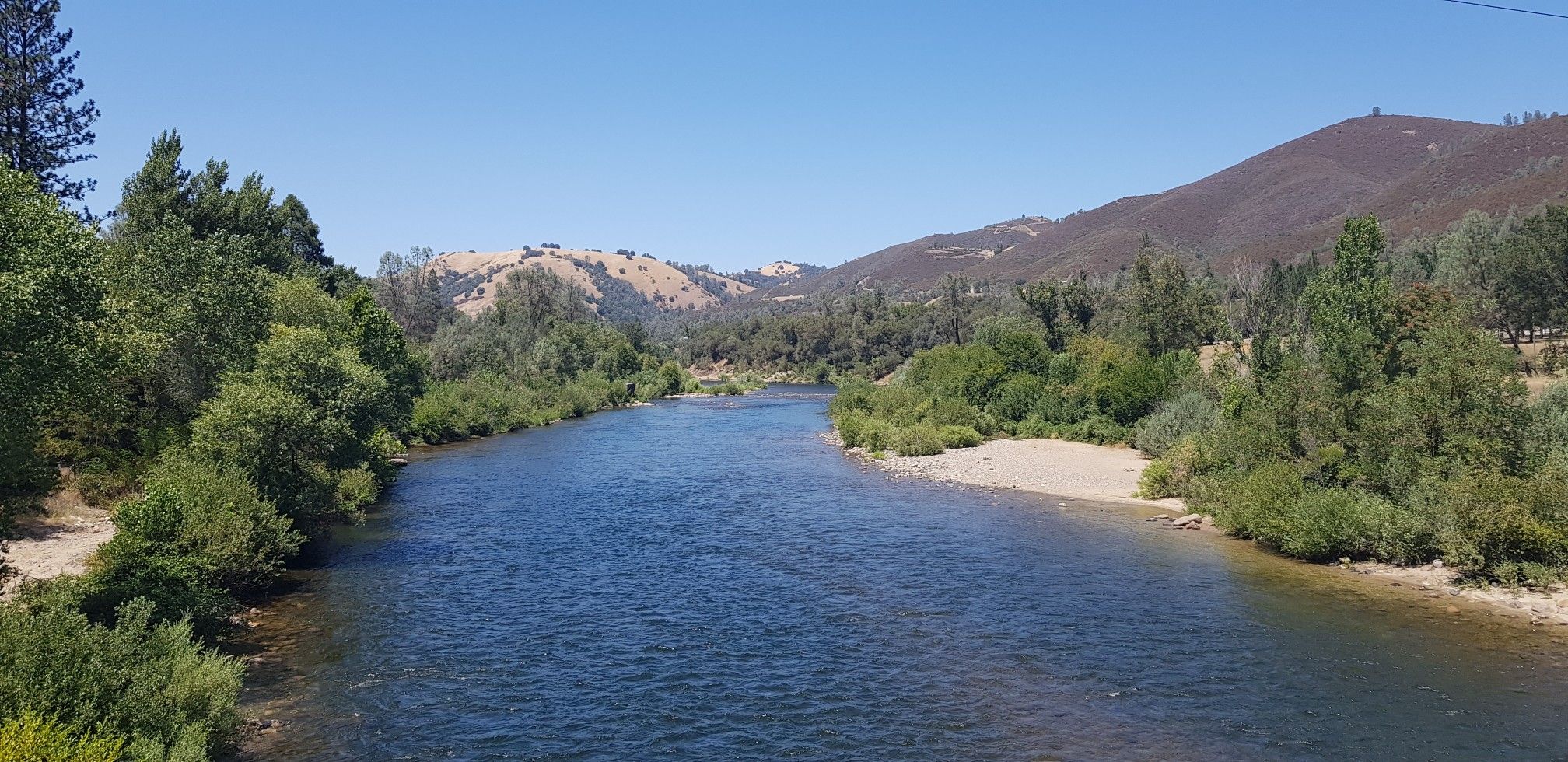 Wide river flows through a green valley under a clear blue sky. - Sutter's Mill loop from Auburn Lake Trails