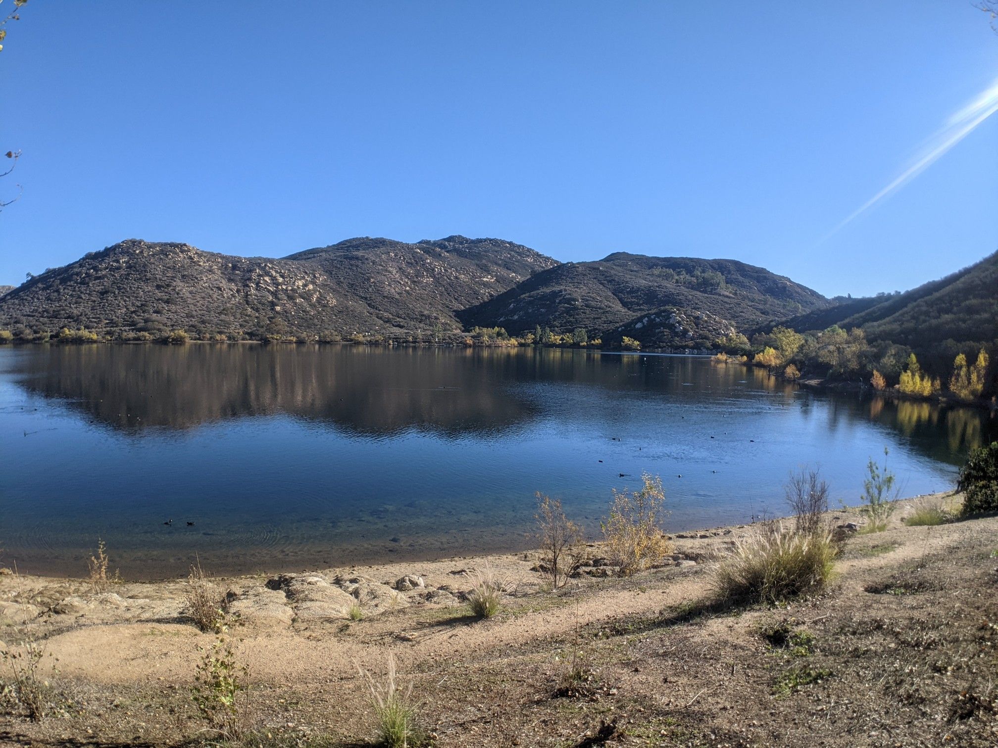 Calm lake reflects rugged mountains under a clear blue sky. - Lake Poway Loop Trail