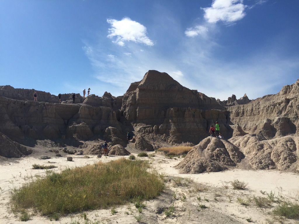 Hikers explore a vast, rugged, sunlit badlands landscape under a blue sky. - Fossil Exhibit Trail