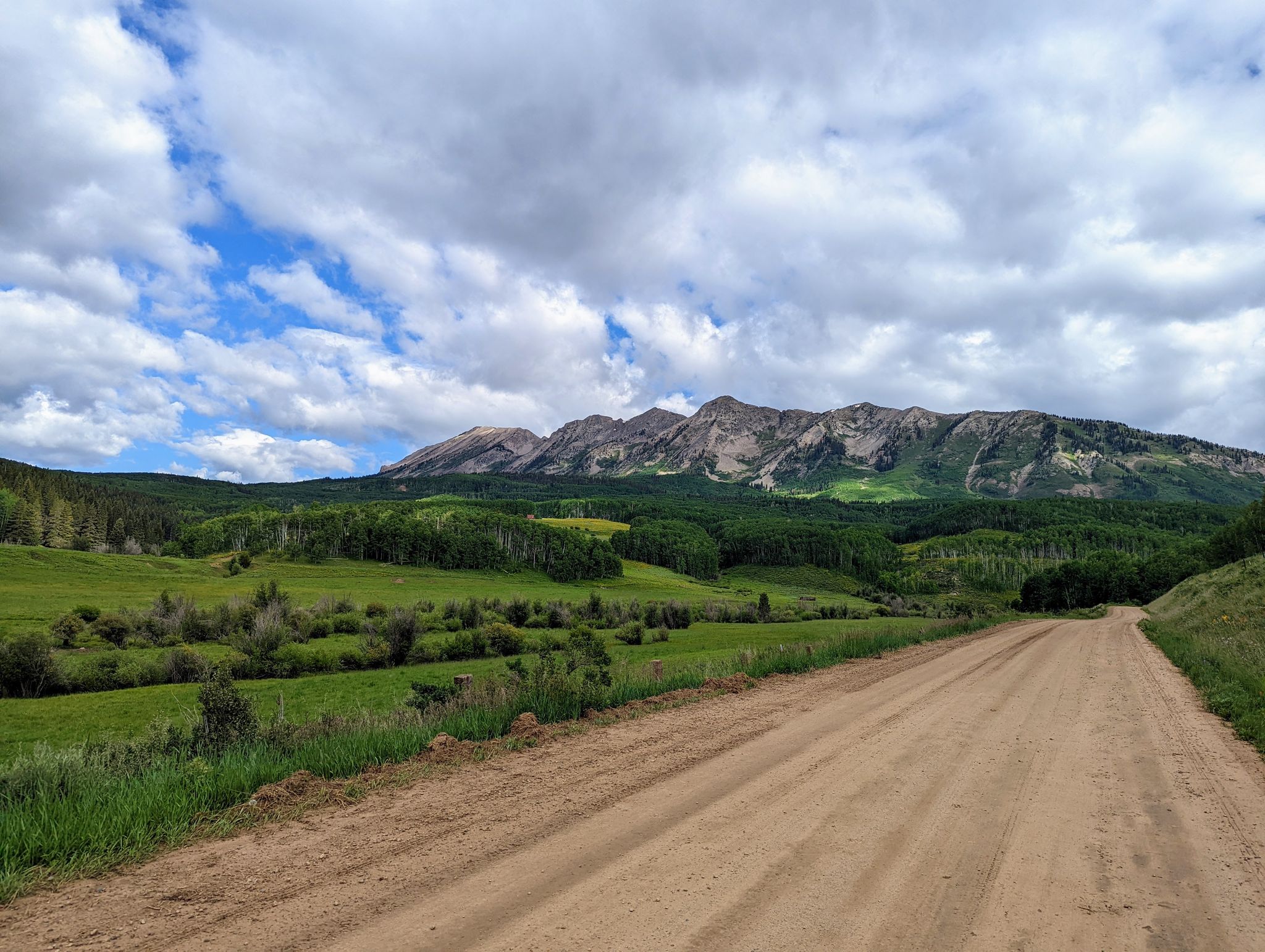 A dirt road leads towards green mountains under a cloudy sky. - Old Ohio Pass Road