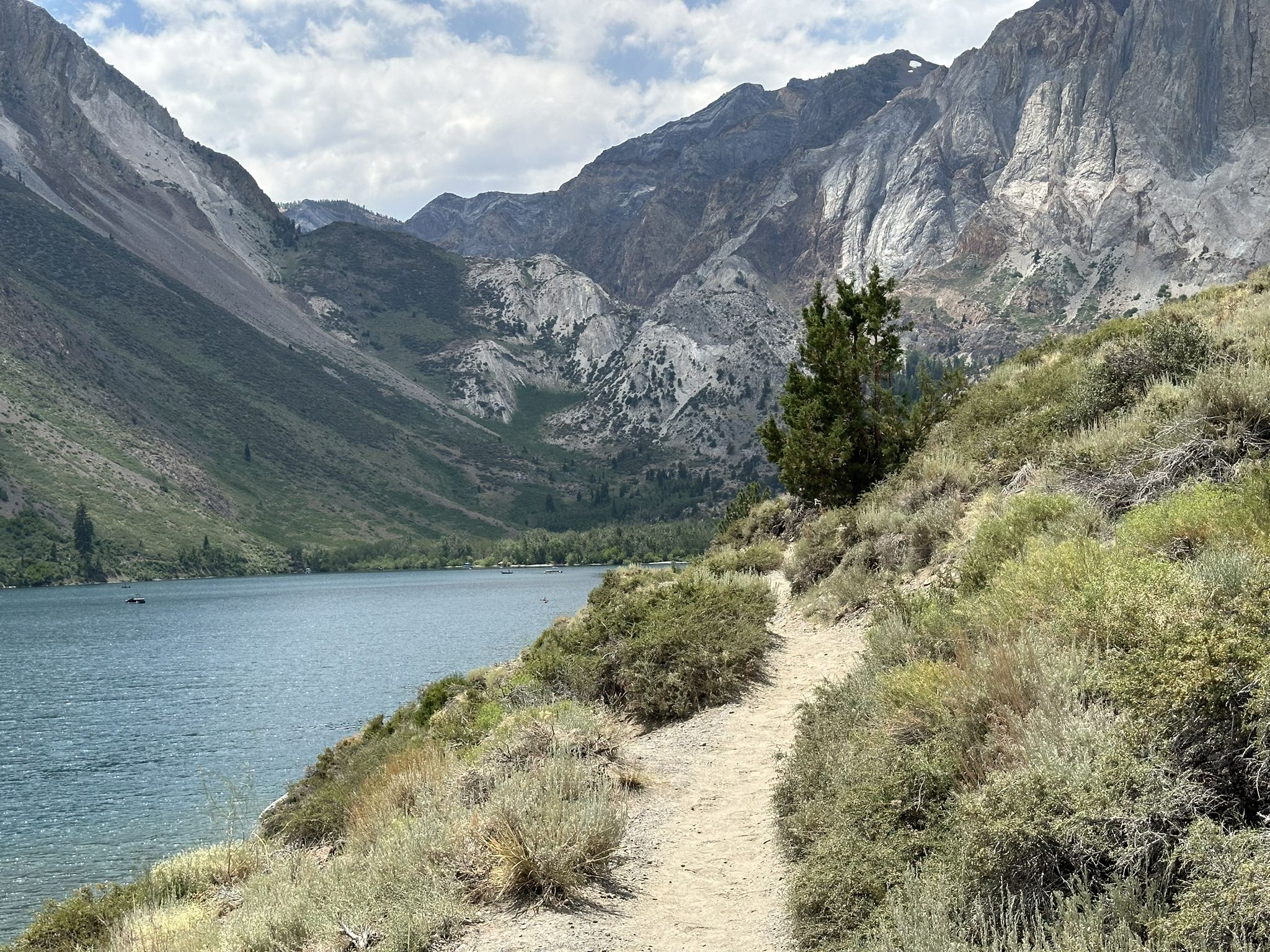 Dirt path alongside a lake with large mountains under a cloudy sky. - Convict Lake Loop