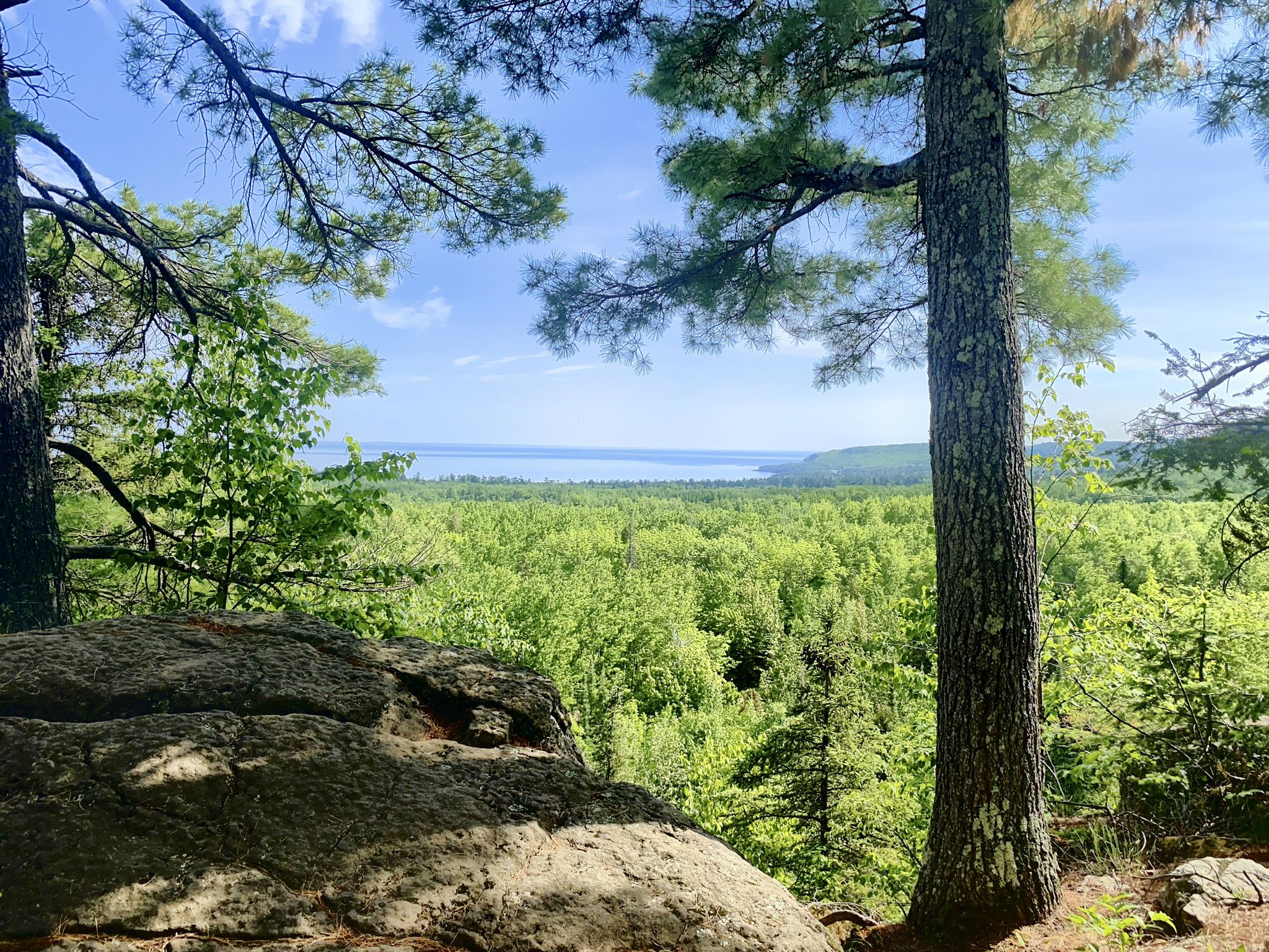 Forest overlook with distant water, large rock in foreground, bright sky. - Superior Hiking Trail