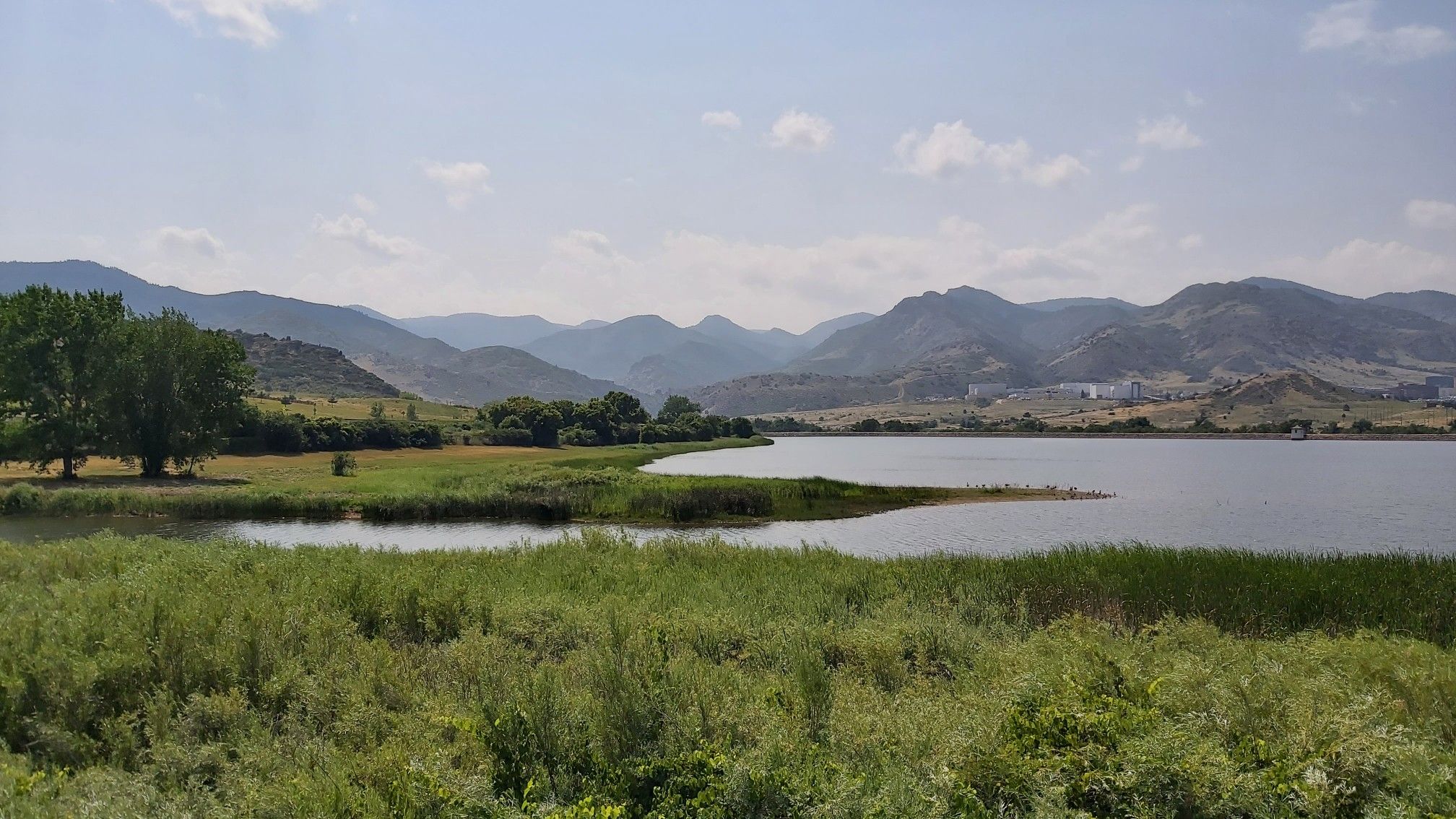 A serene lake with green banks and distant mountains under a bright sky. - Colorado Front Range Trail: Chatfield State Park Loop