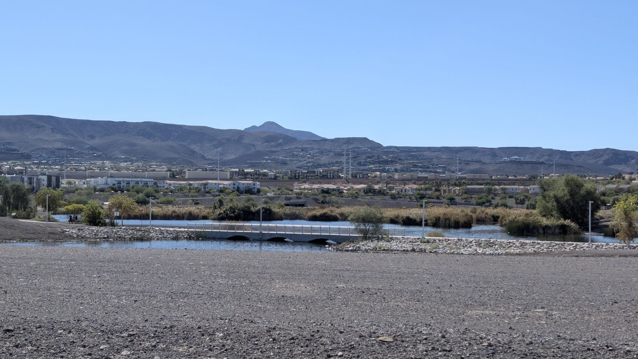 A wide view of a lake with a bridge, distant mountains, and buildings. - Harry Reid UPRR and Pittman Wash Trails Loop