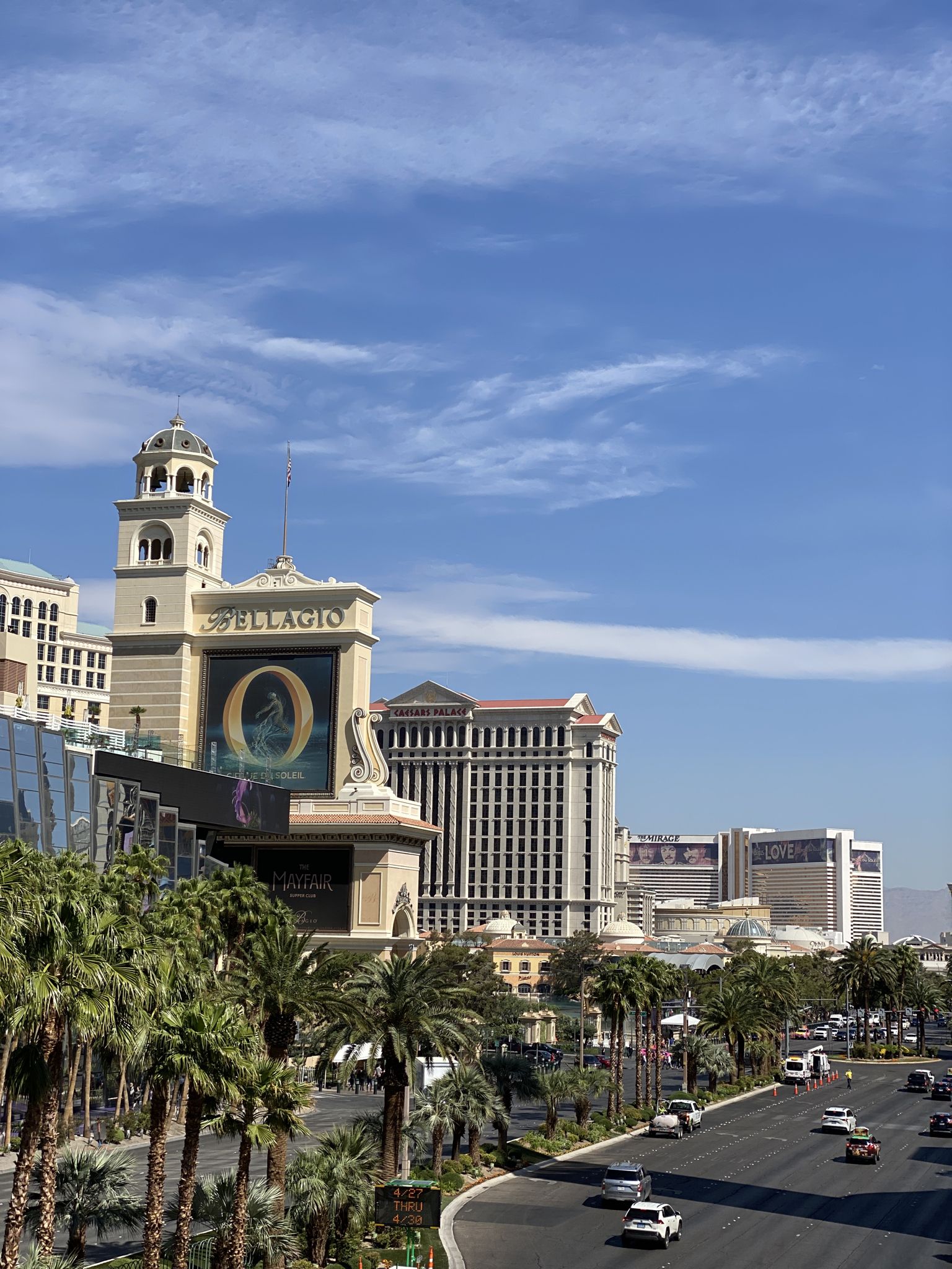 Cityscape with large buildings, palm trees, and a busy road under a blue sky. - The Strip