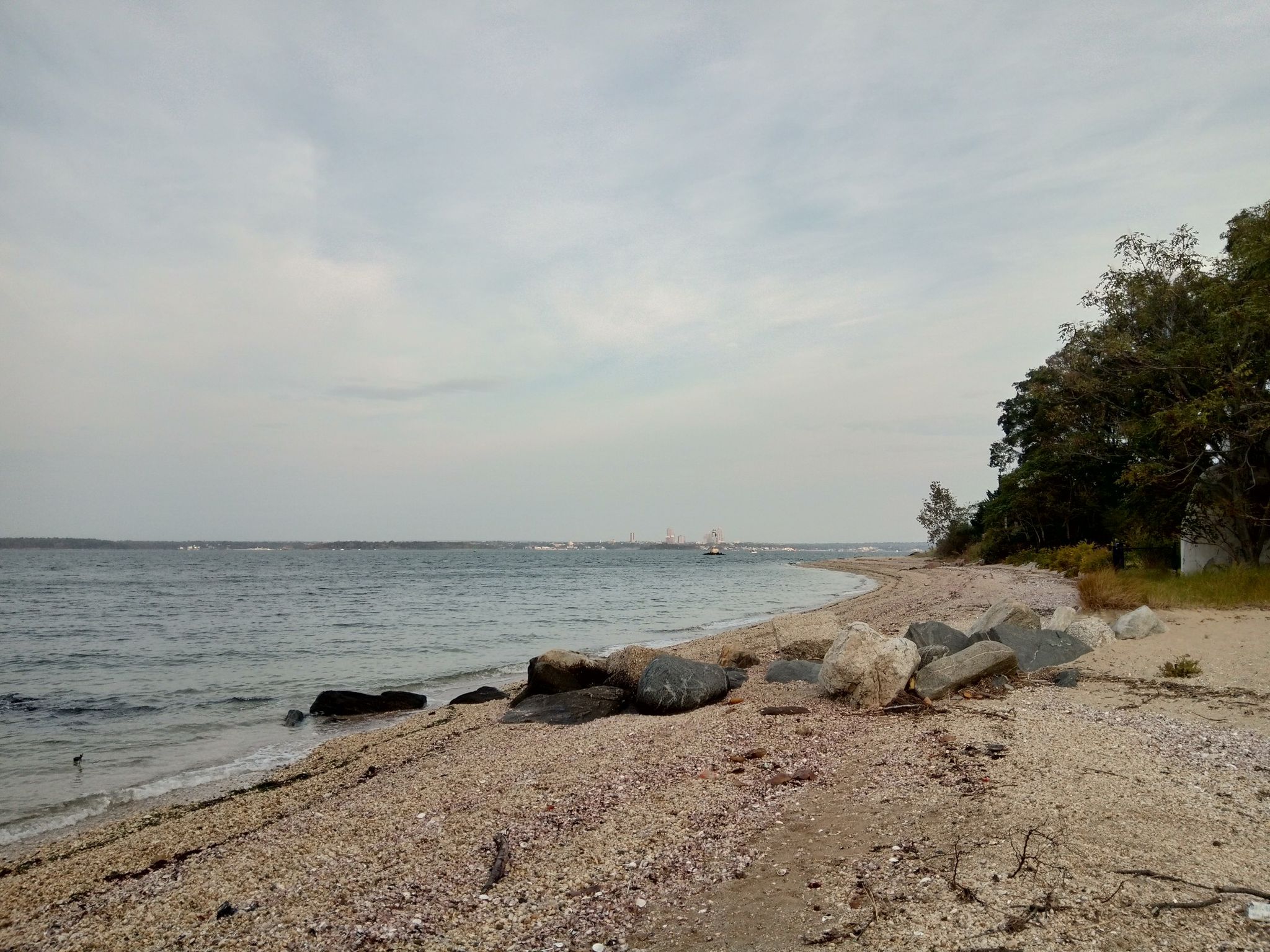 A rocky and sandy beach meets calm ocean water under an overcast sky. - Great Neck Double Loop