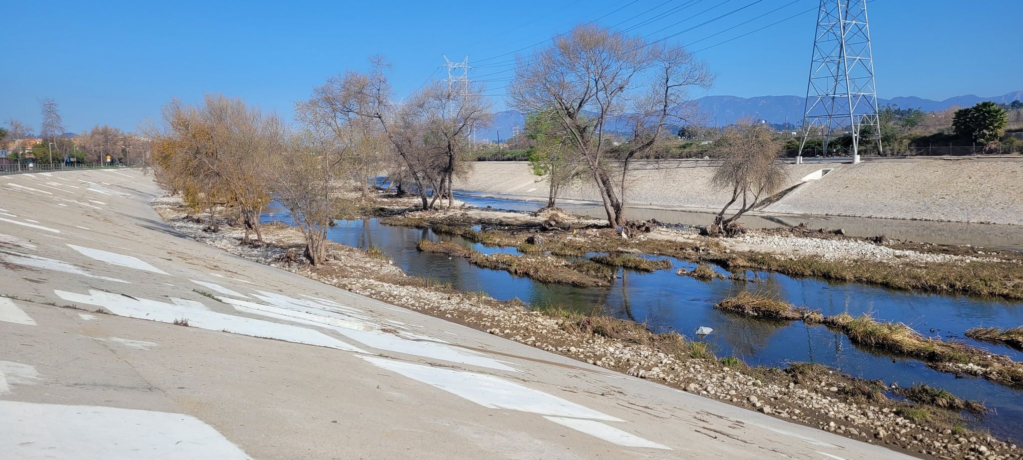 A narrow river flows between concrete banks with sparse trees on a clear day. - Los Angeles River Greenway and Griffith Park Loop