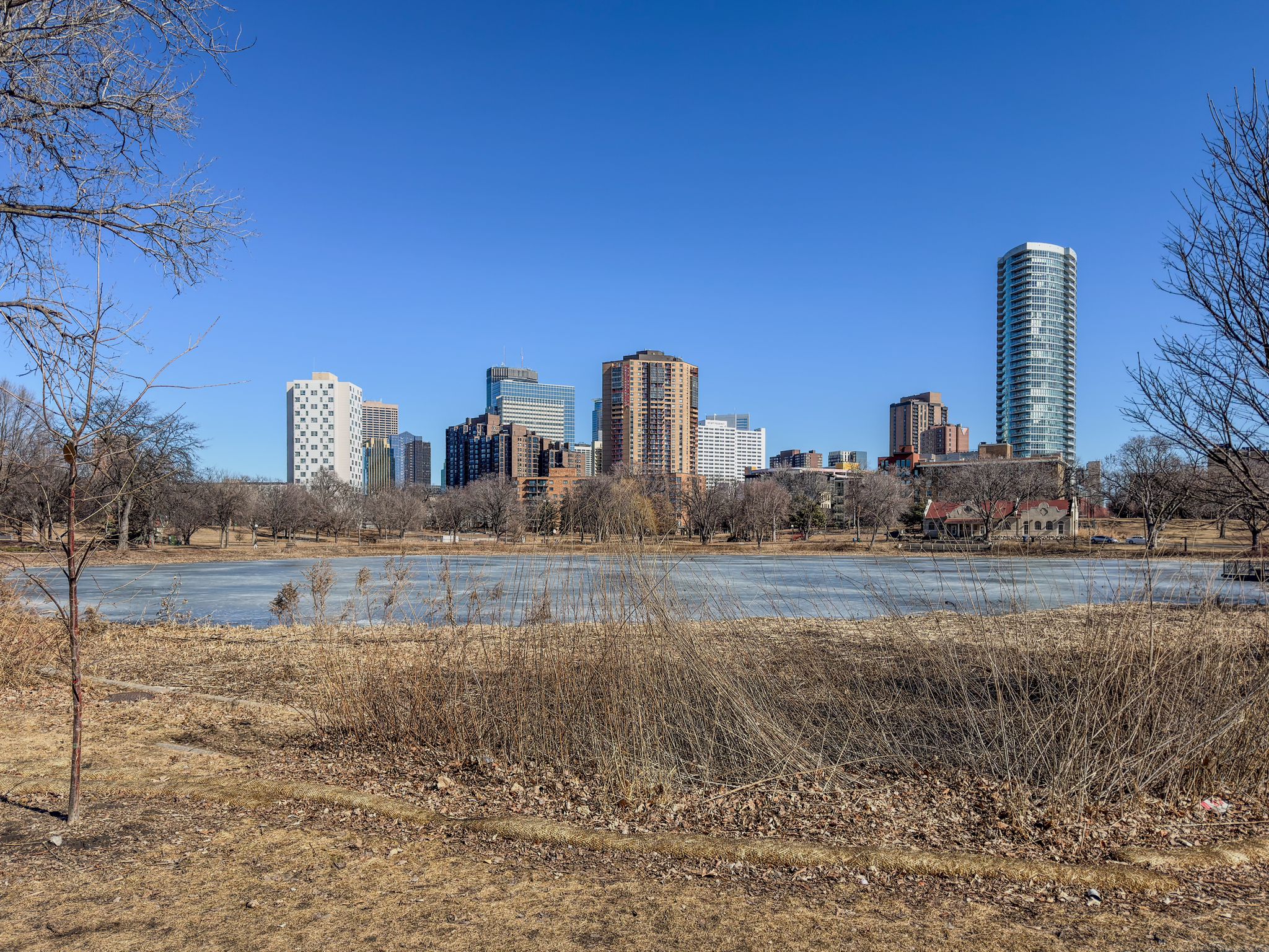 City skyline across a partially frozen lake with bare trees under clear sky. - Loring Park Loop