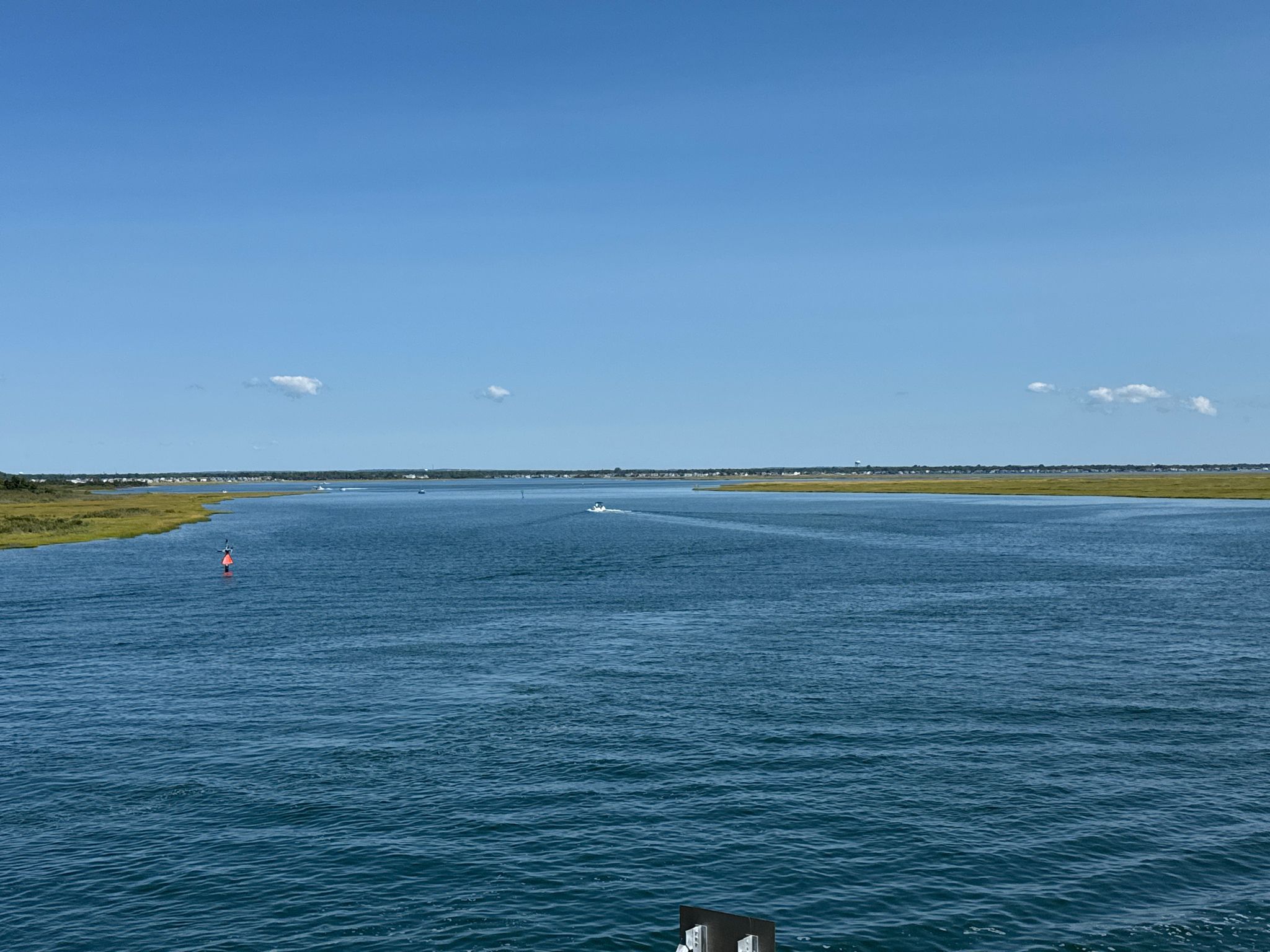 Wide waterway with marshlands under a clear blue sky, distant boat. - Ocean Parkway Coastal Greenway