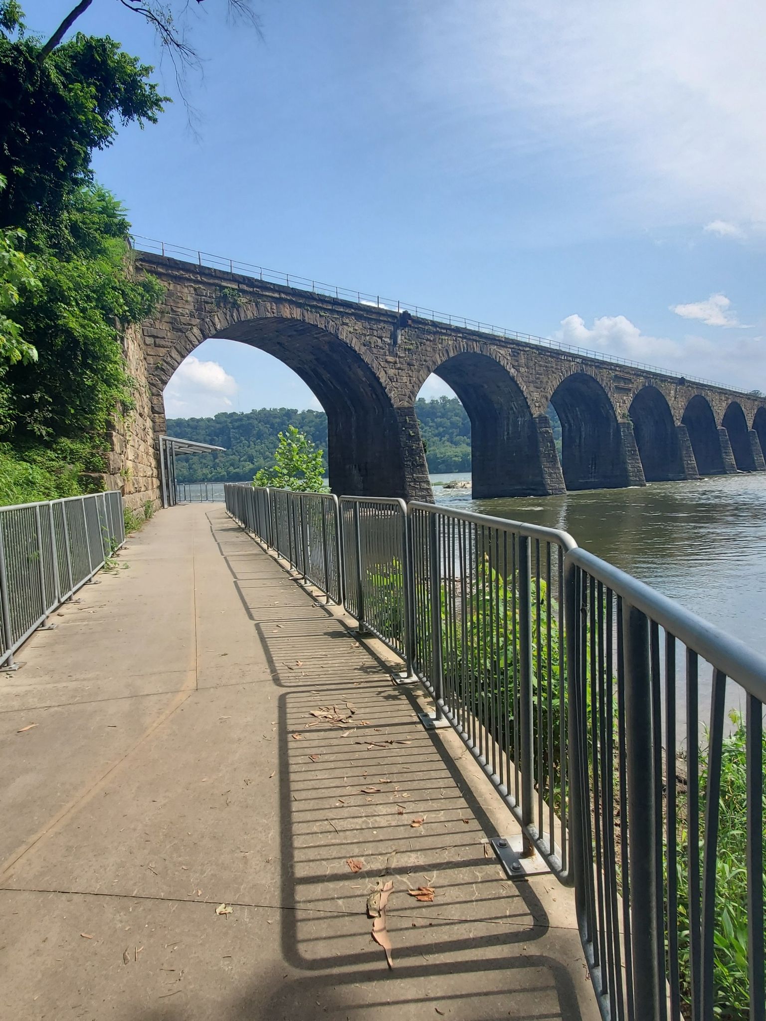 Paved path with railing alongside a wide river and a long stone arch bridge. - White Cliffs of Conoy – Safe Harbor Railroad Bridge loop from York Haven