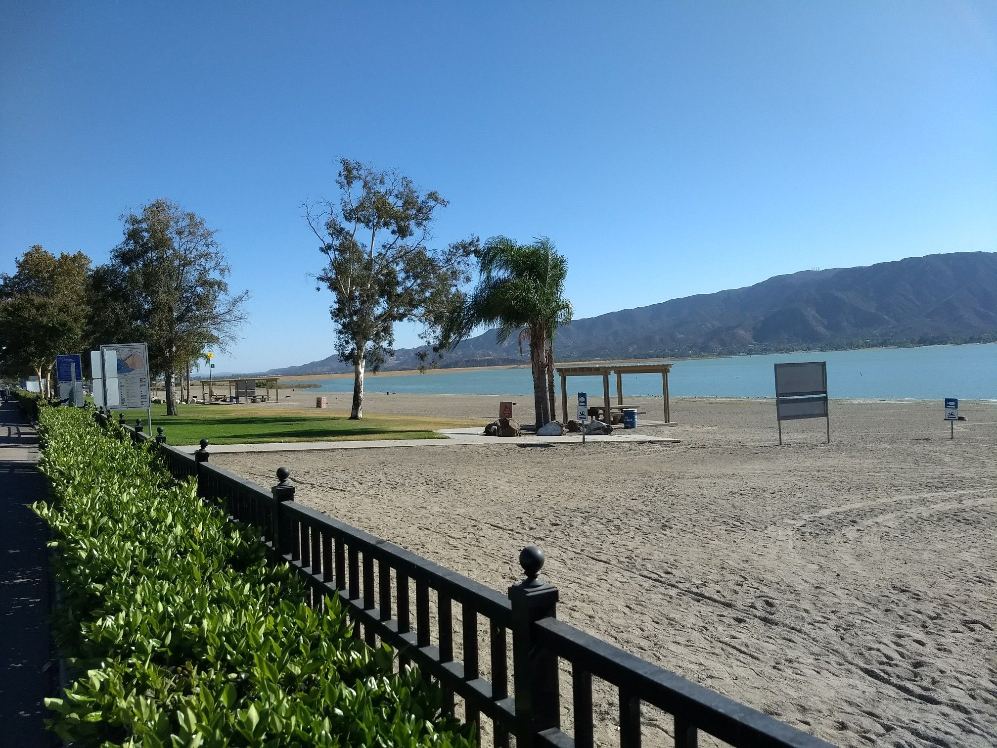 Sunny beach scene with a lake, distant mountains, and green trees. - Historic Downtown Riverwalk (Temescal Wash Trail) loop