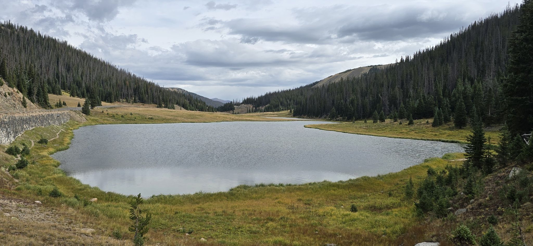 A calm lake surrounded by forested mountains under a cloudy sky. - Mount Ida Trail