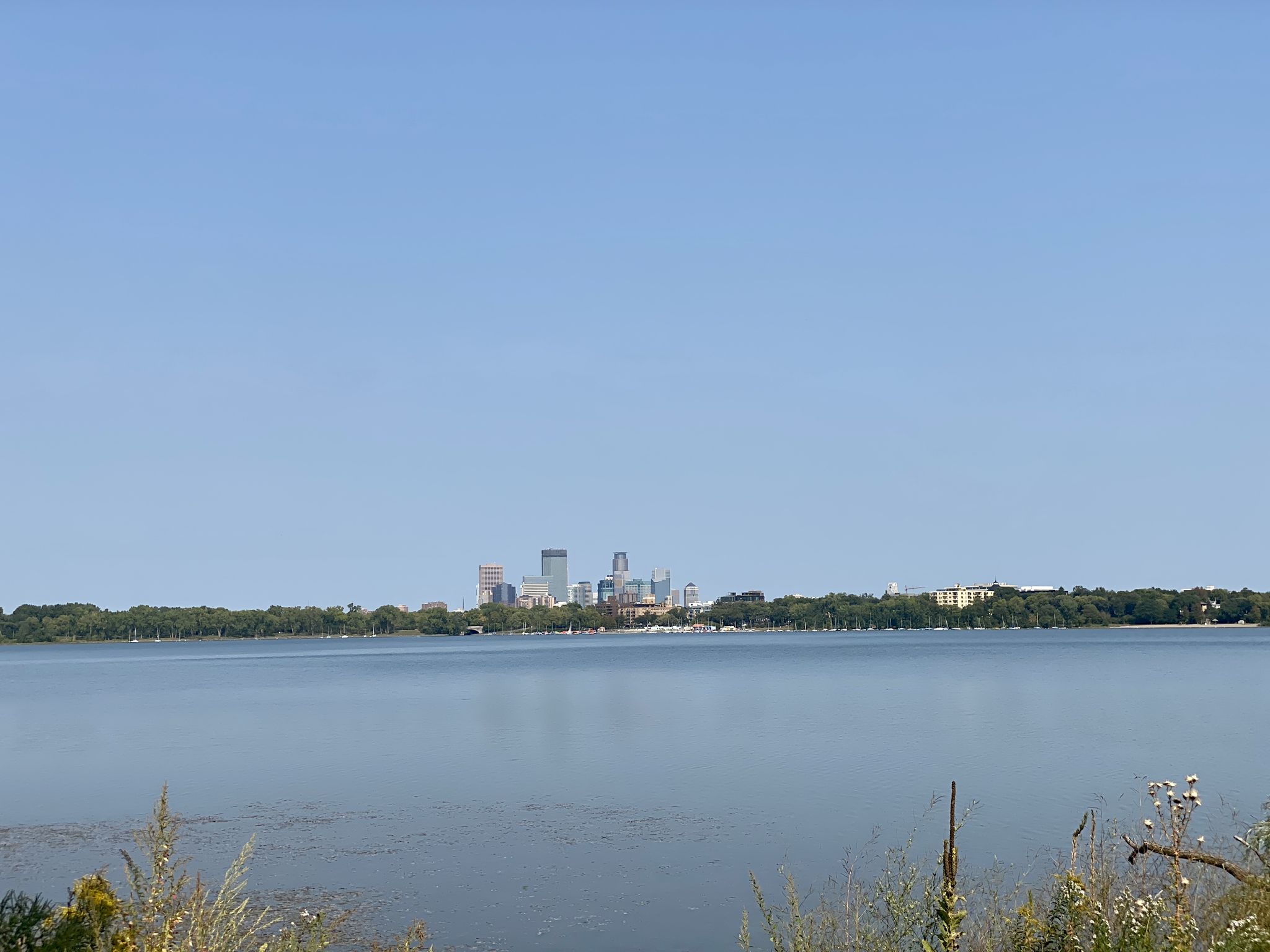 Calm lake with a distant city skyline under a clear blue sky. - Bde Maka Ska – Thomas Beach loop from Linden Hills