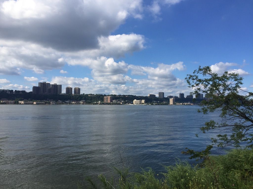 Wide river with a distant city skyline under a bright, cloudy sky. - Cherry Walk