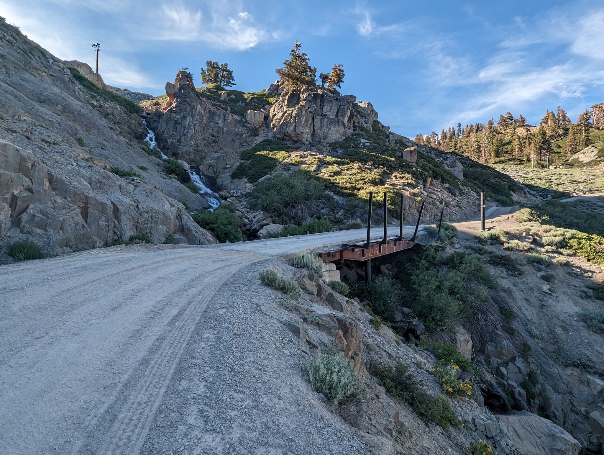 Dirt road on a rocky mountain slope, with a small waterfall and wooden bridge. - Western States Trail Loop