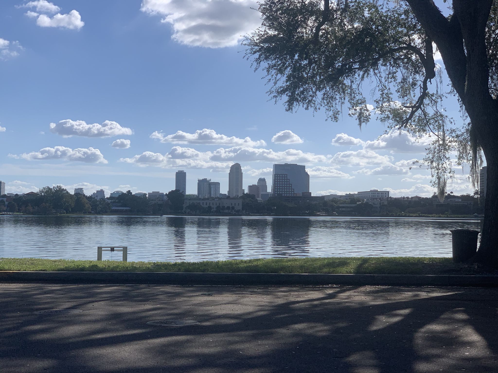 A city skyline visible across a wide lake on a bright, cloudy day. - Gaston Edwards Park loop