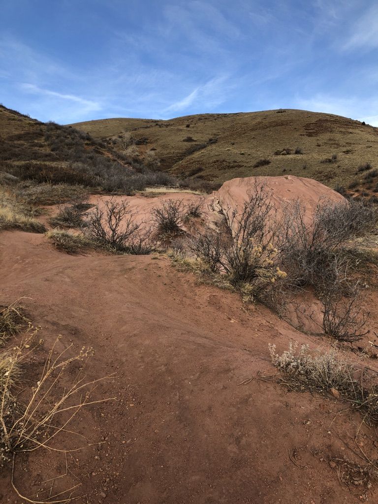 Red dirt trail winding past large red rocks and dry hills under blue sky. - Red Rocks Trail to Cherry Gulch Loop