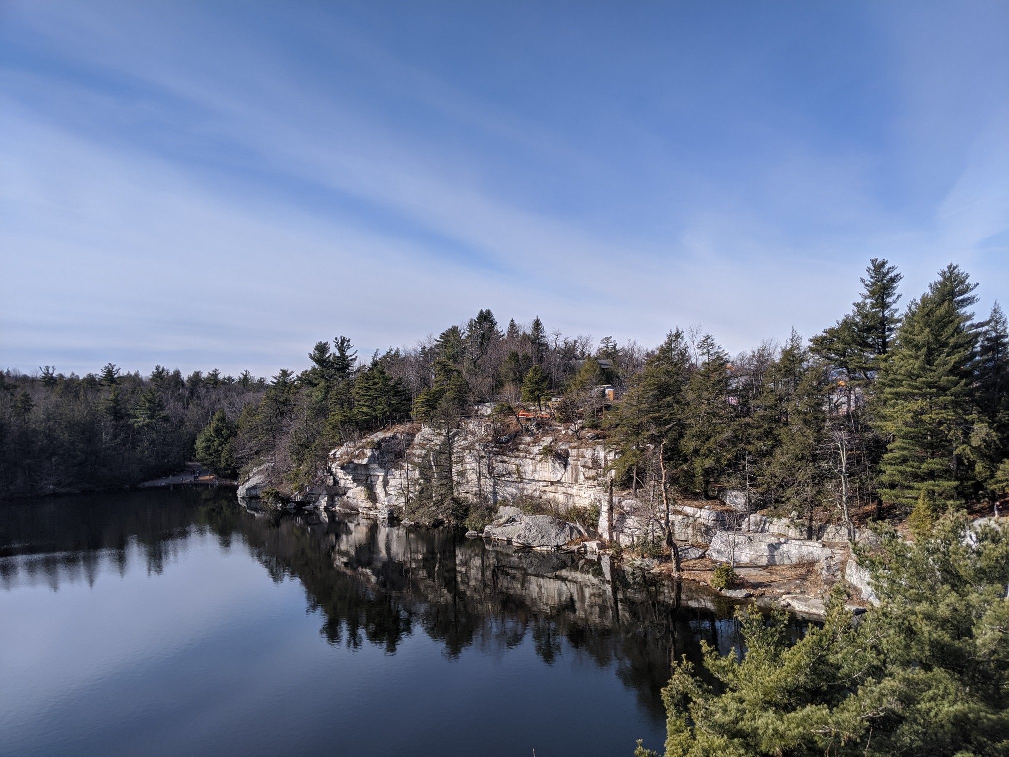 A dark lake bordered by rocky cliffs and dense pine forests under a clear sky. - Gertrude's Nose and Millbrook Mountain Loop